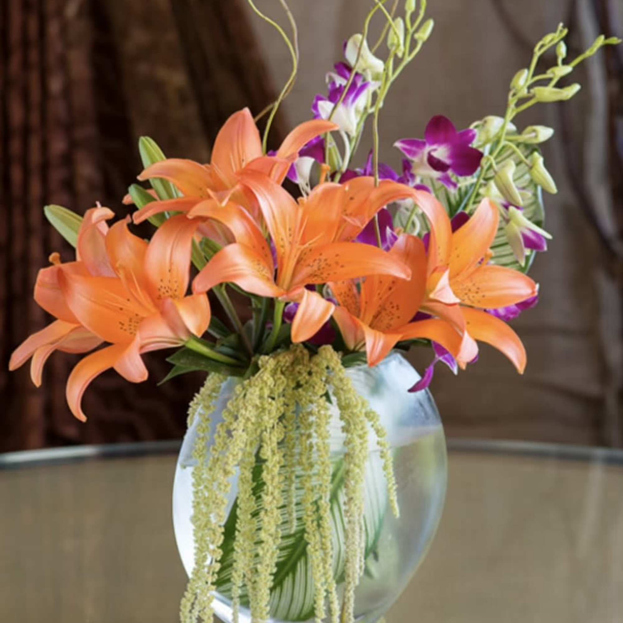Orange lilies and purple orchids in a clear glass vase, photo 3 of 5