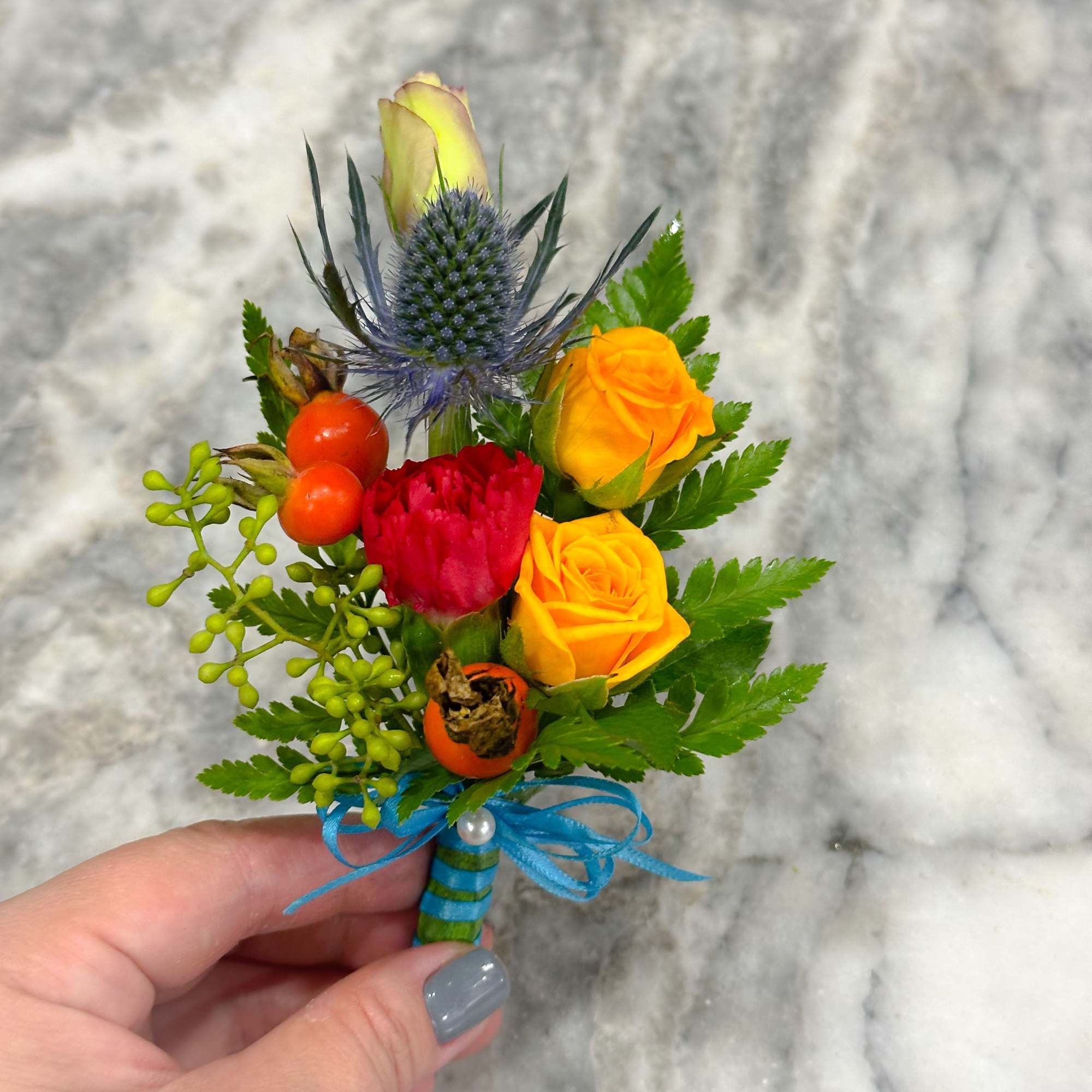 Small boutonniere with yellow and red roses and blue thistle