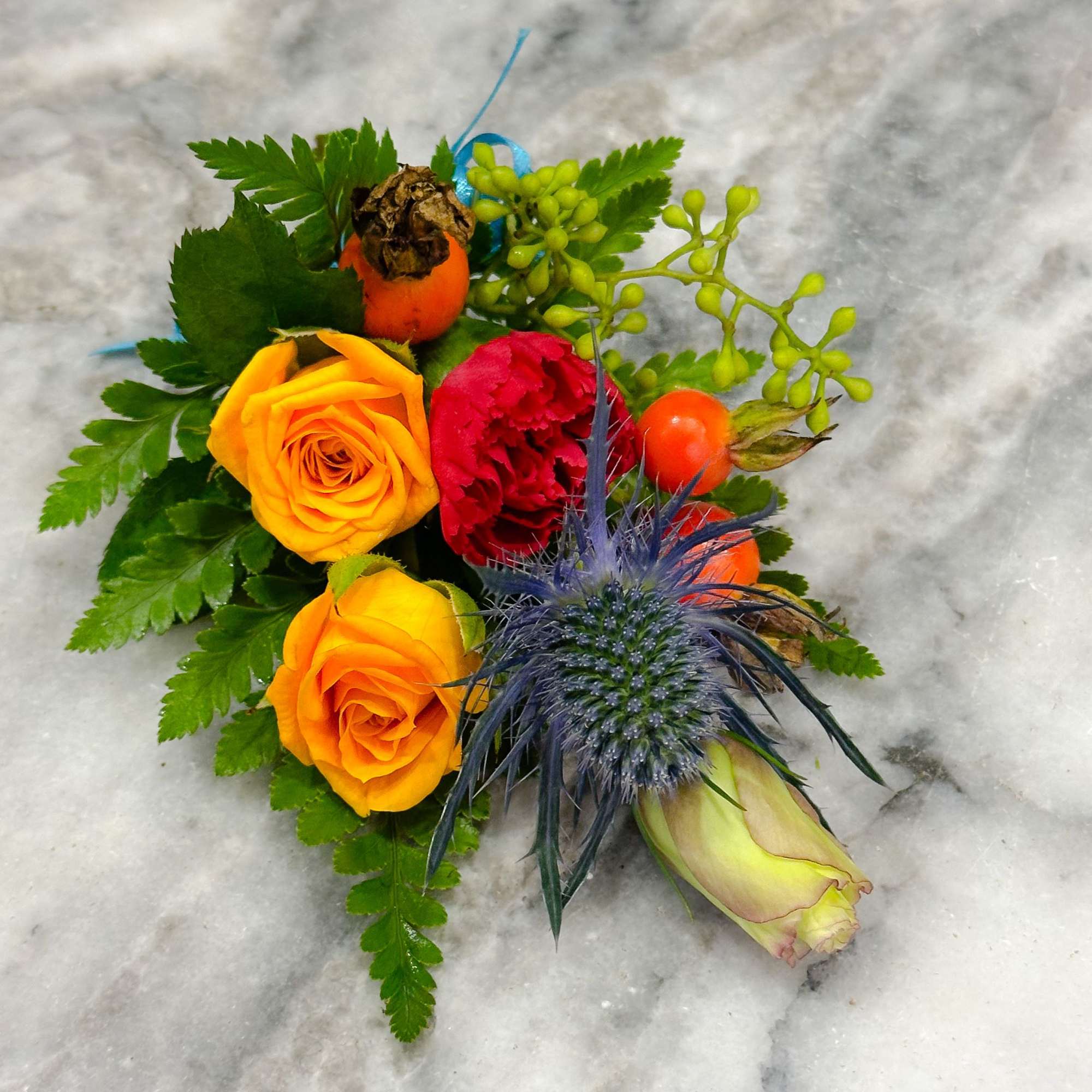 Small floral arrangement with orange and red roses and a blue thistle bloom