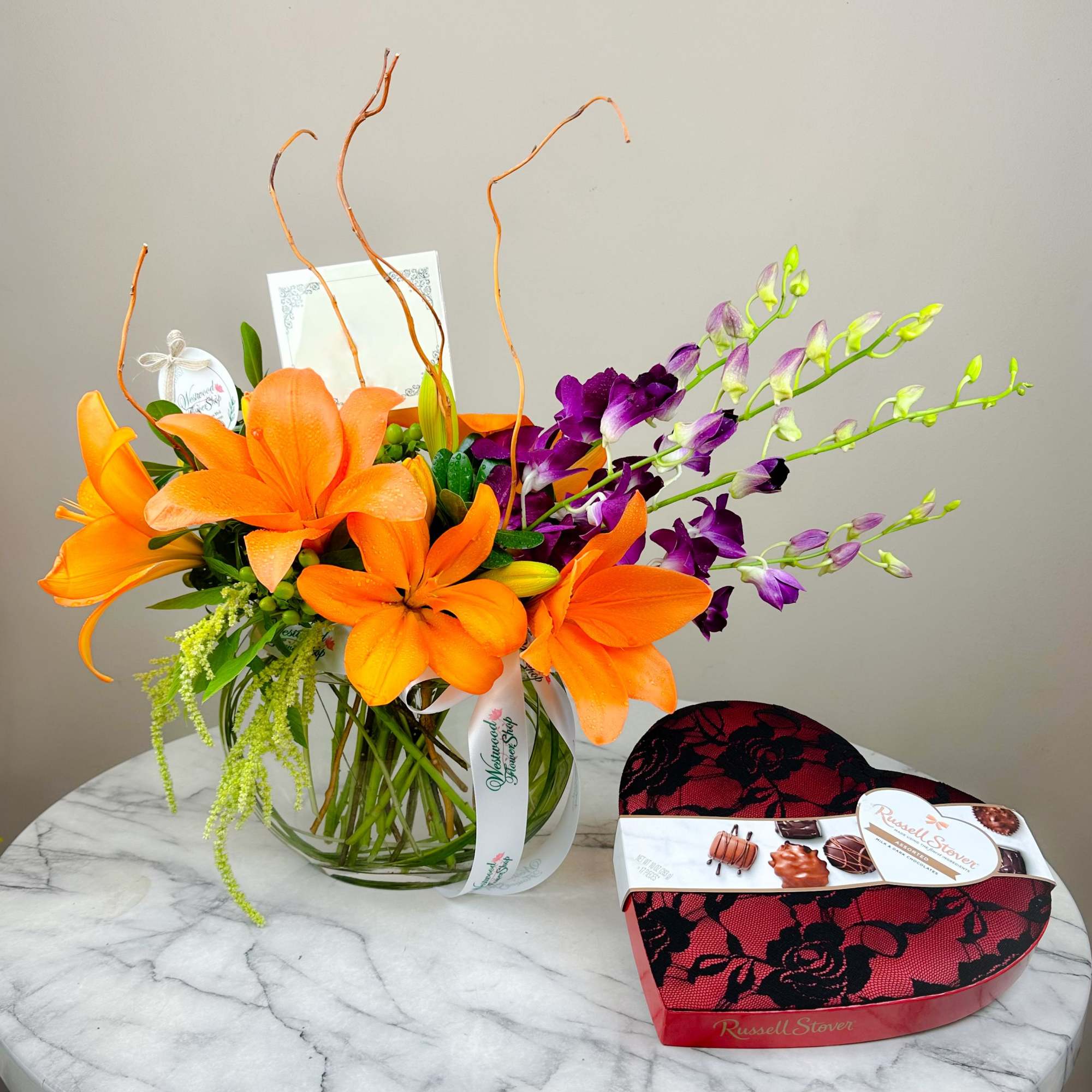 Orange lilies in a glass vase beside a heart-shaped chocolate box