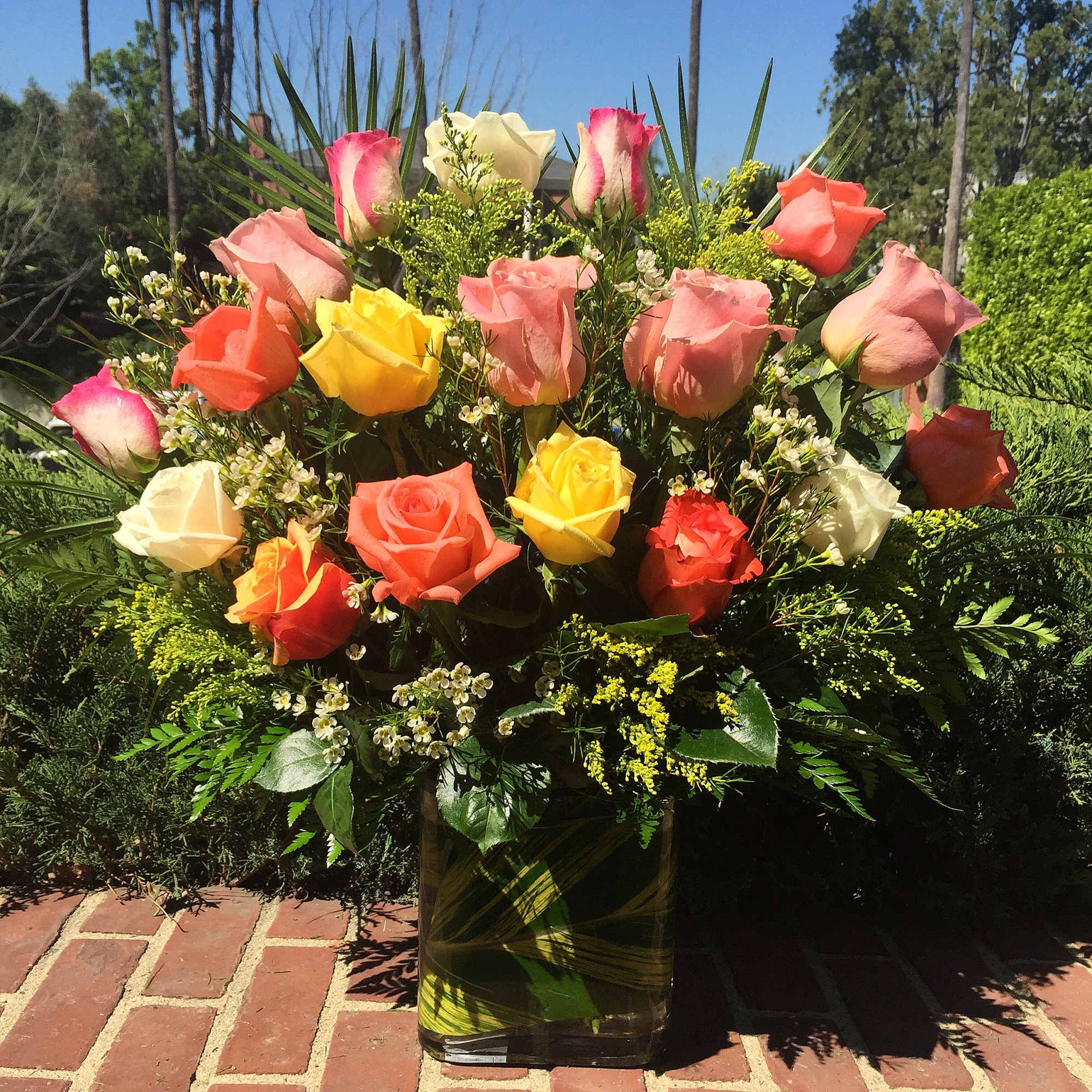 Mixed roses in a glass vase with yellow filler flowers