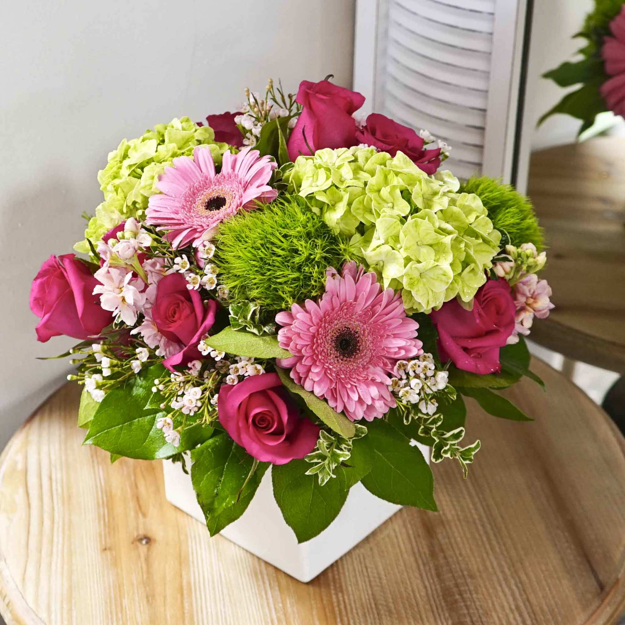 Pink roses and gerbera daisies in a white square vase with green hydrangeas