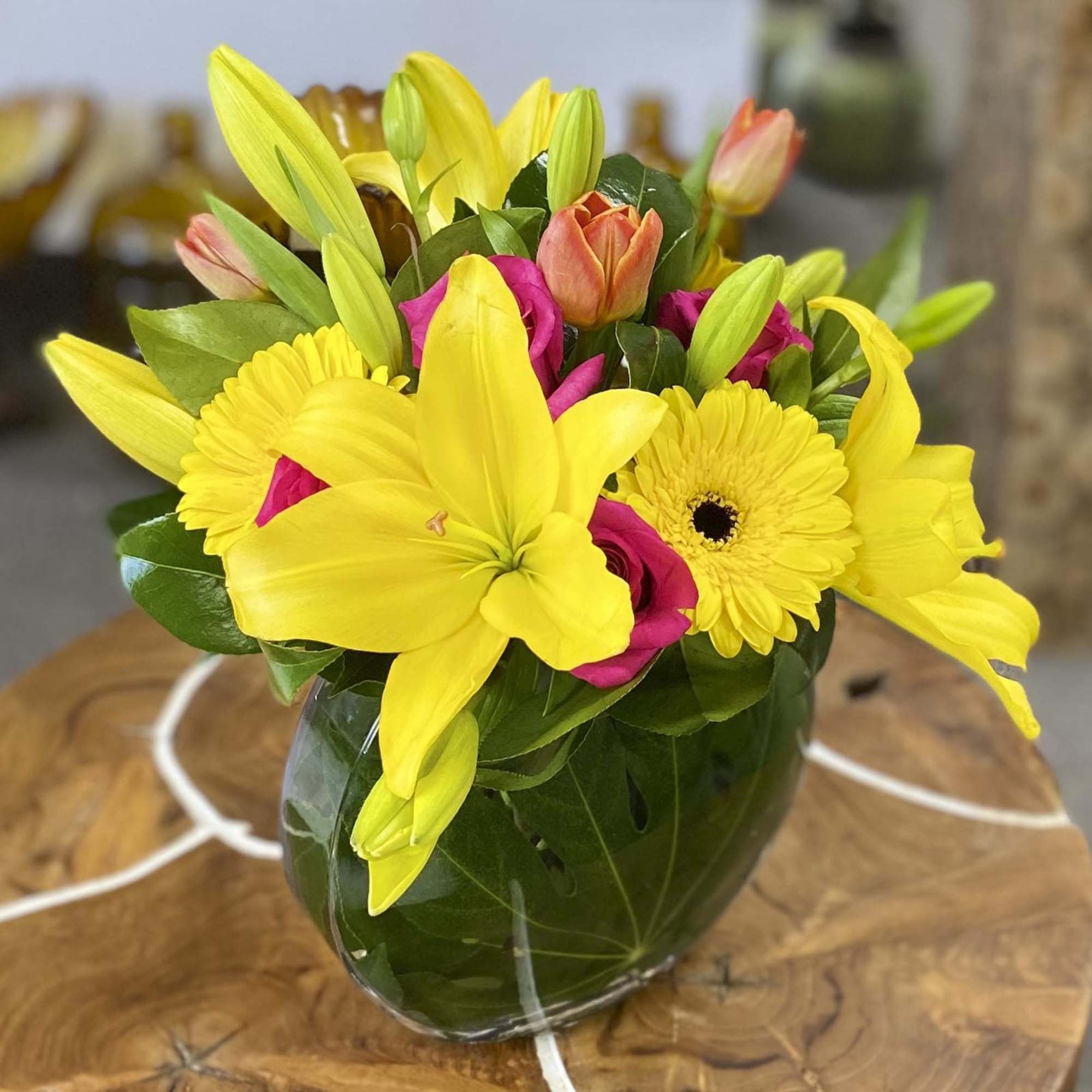 Bright yellow lilies and pink flowers arranged in a glass vase