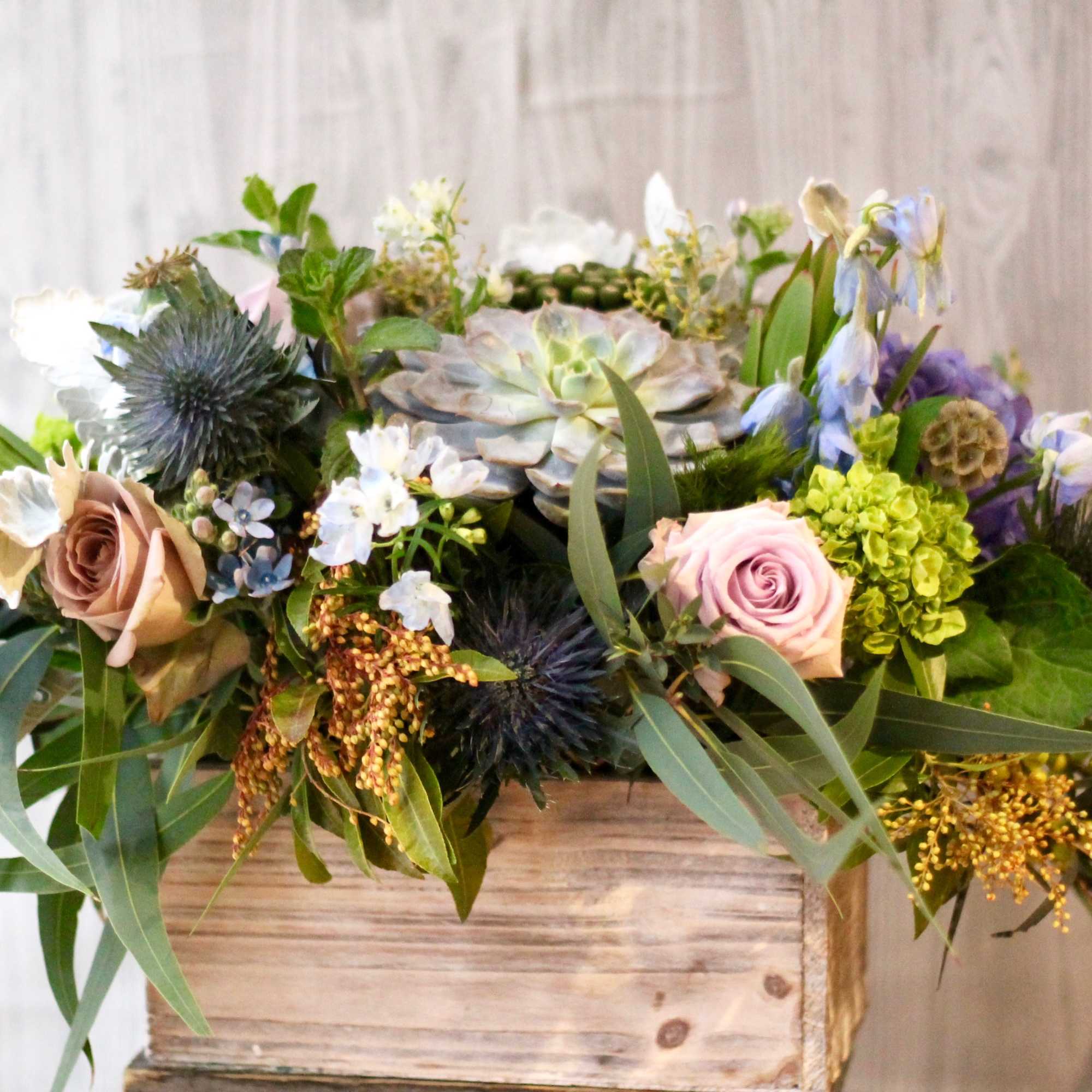 Mixed floral arrangement in a wooden box with roses and succulents