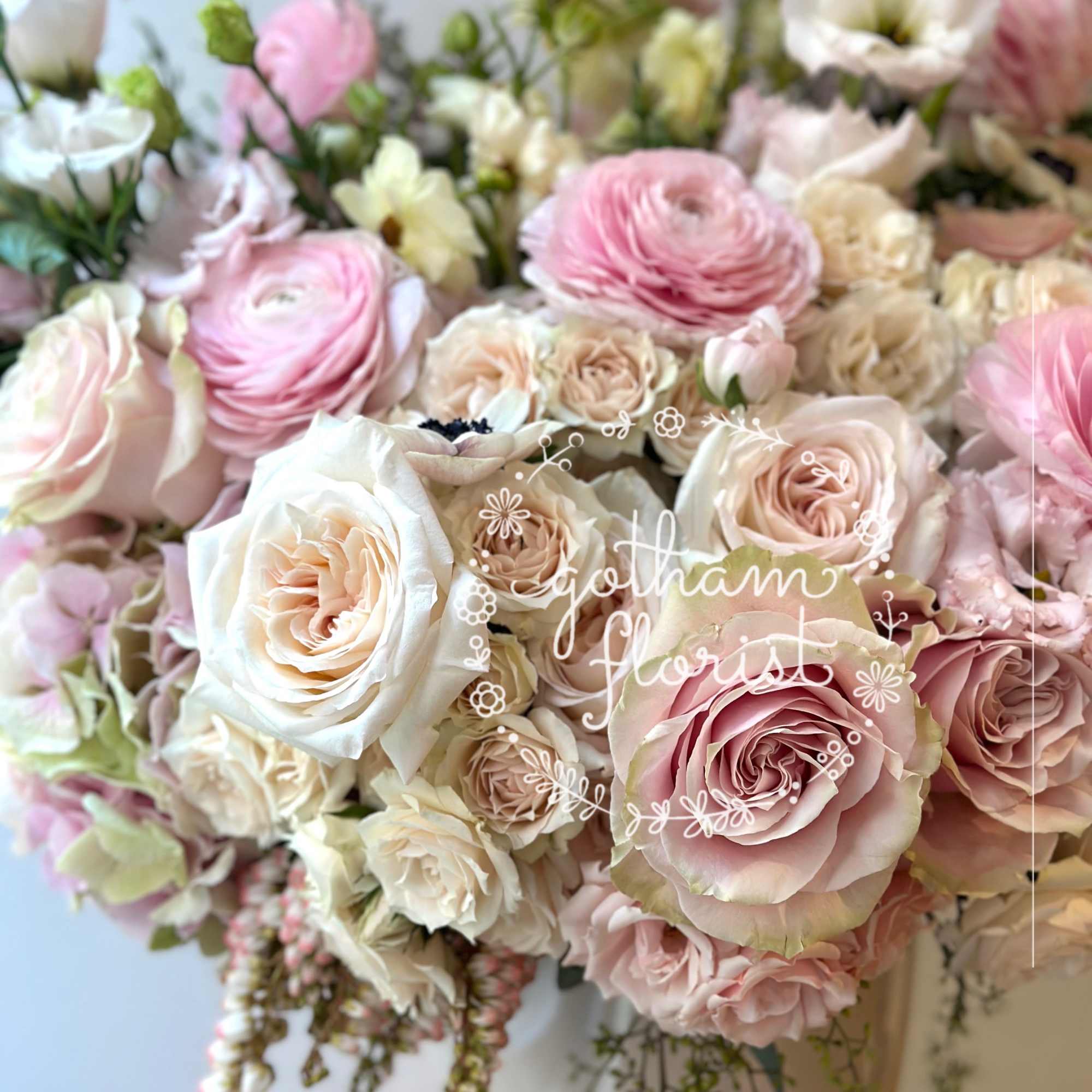 Low bowl arrangement of blush and cream roses, ranunculus, and lisianthus in a white vase