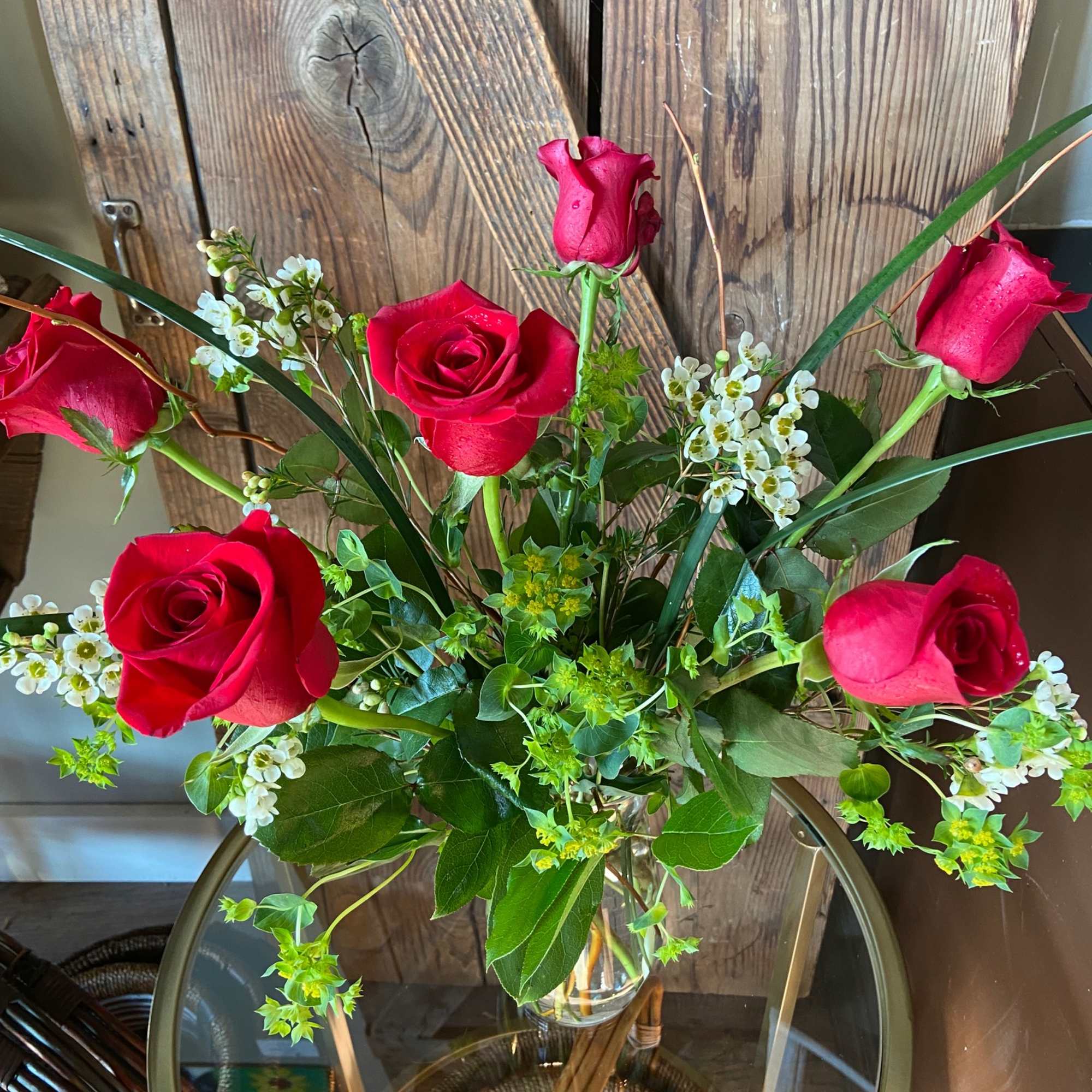 Vase arrangement of red roses with small white blossoms on a round glass table