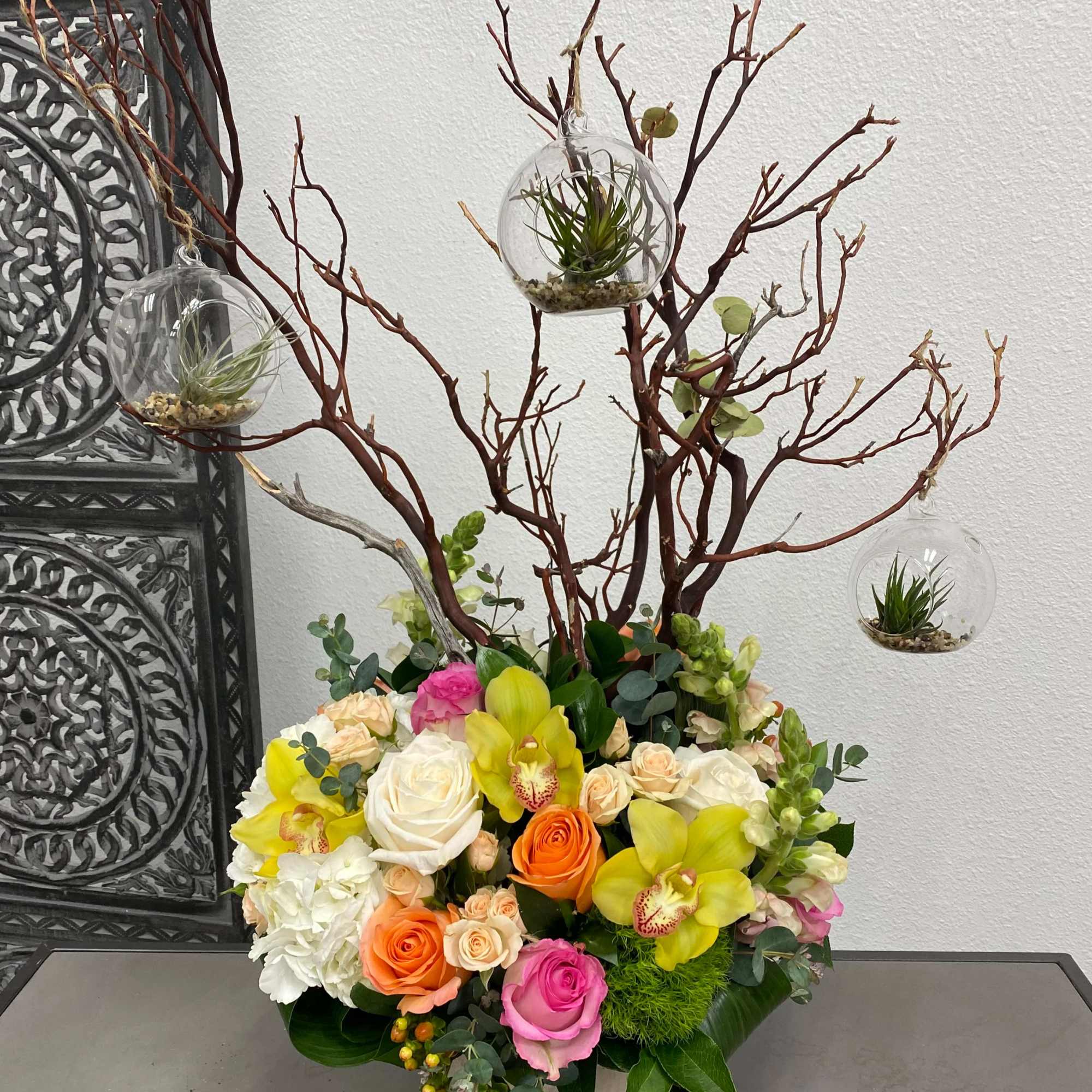 This arrangement includes a vibrant variety of flowers and a manzanita branch