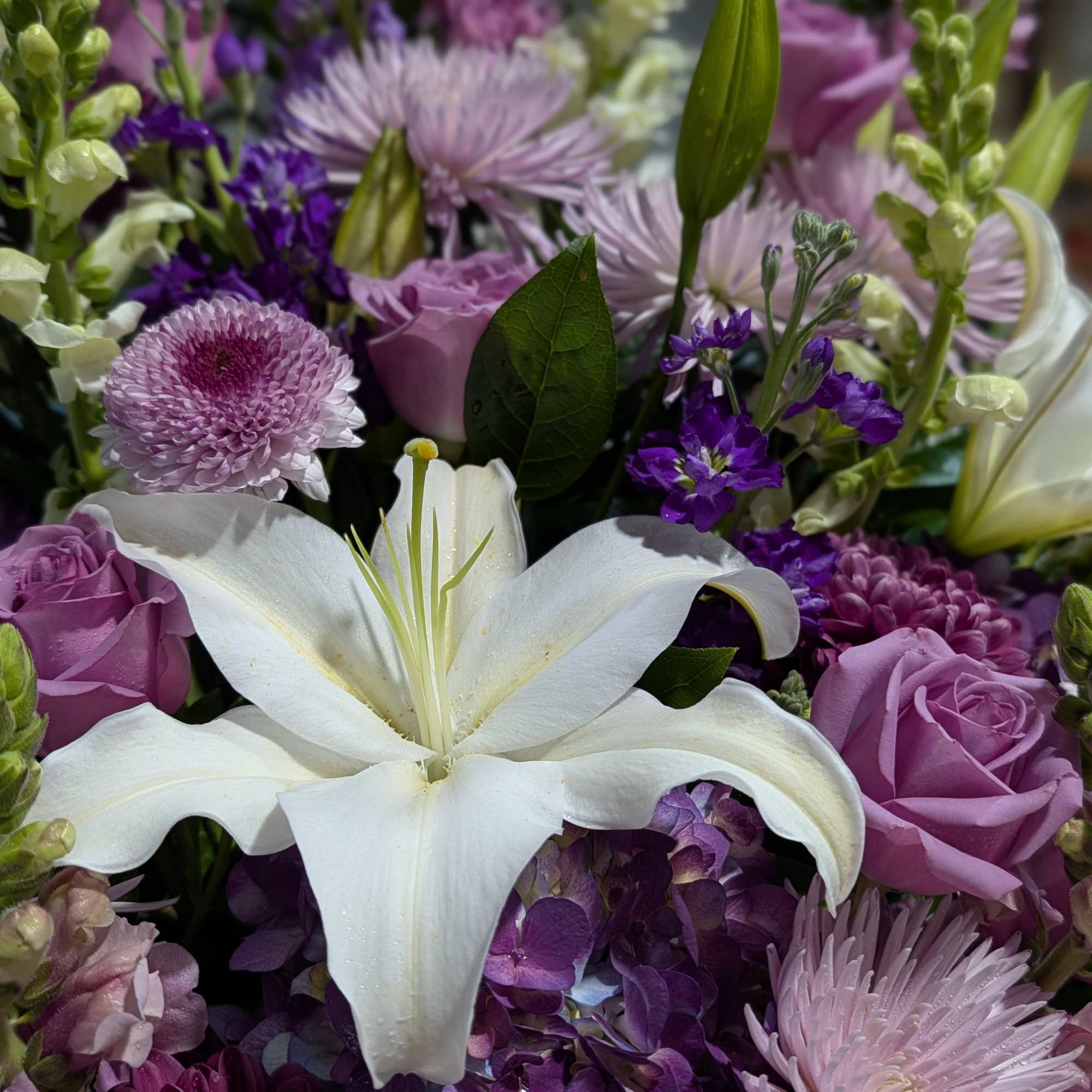White lily surrounded by purple roses and lavender blooms