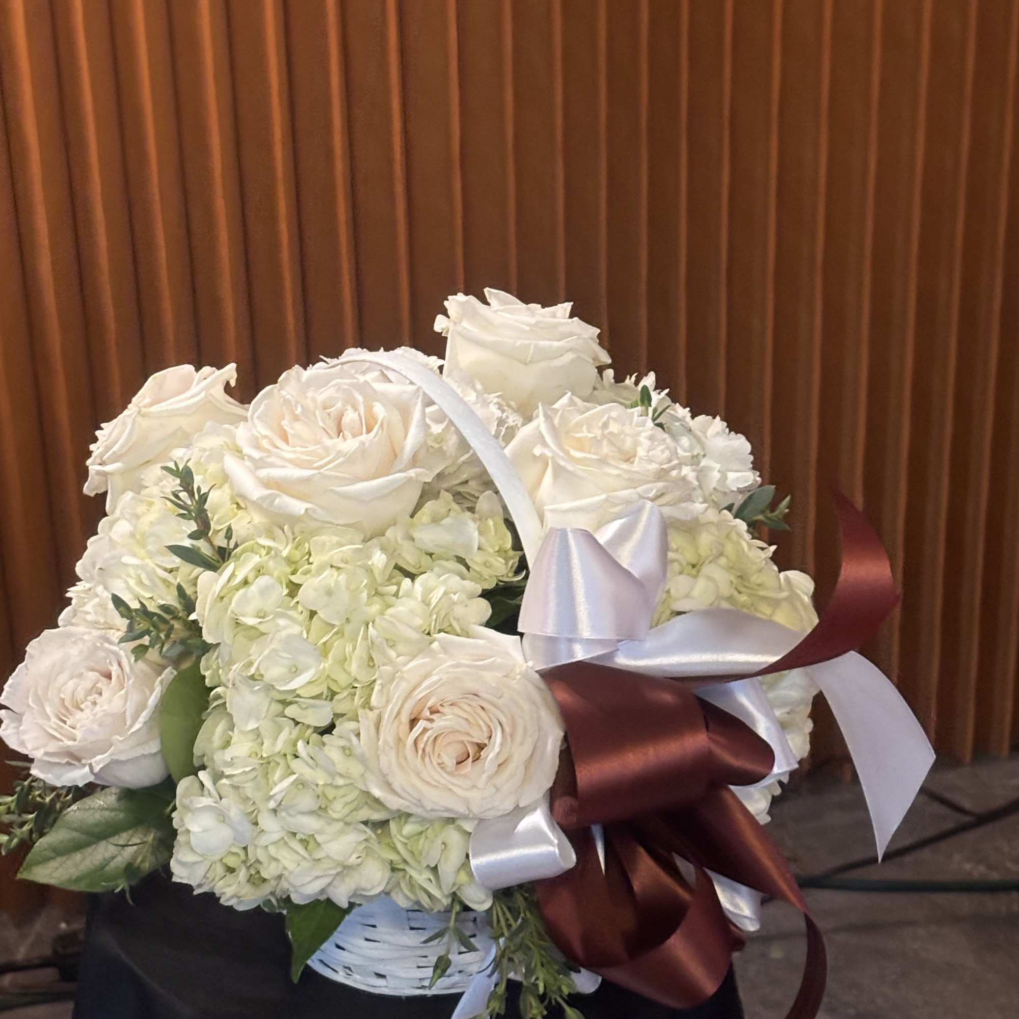 White rose and hydrangea bouquet in a basket with satin ribbons