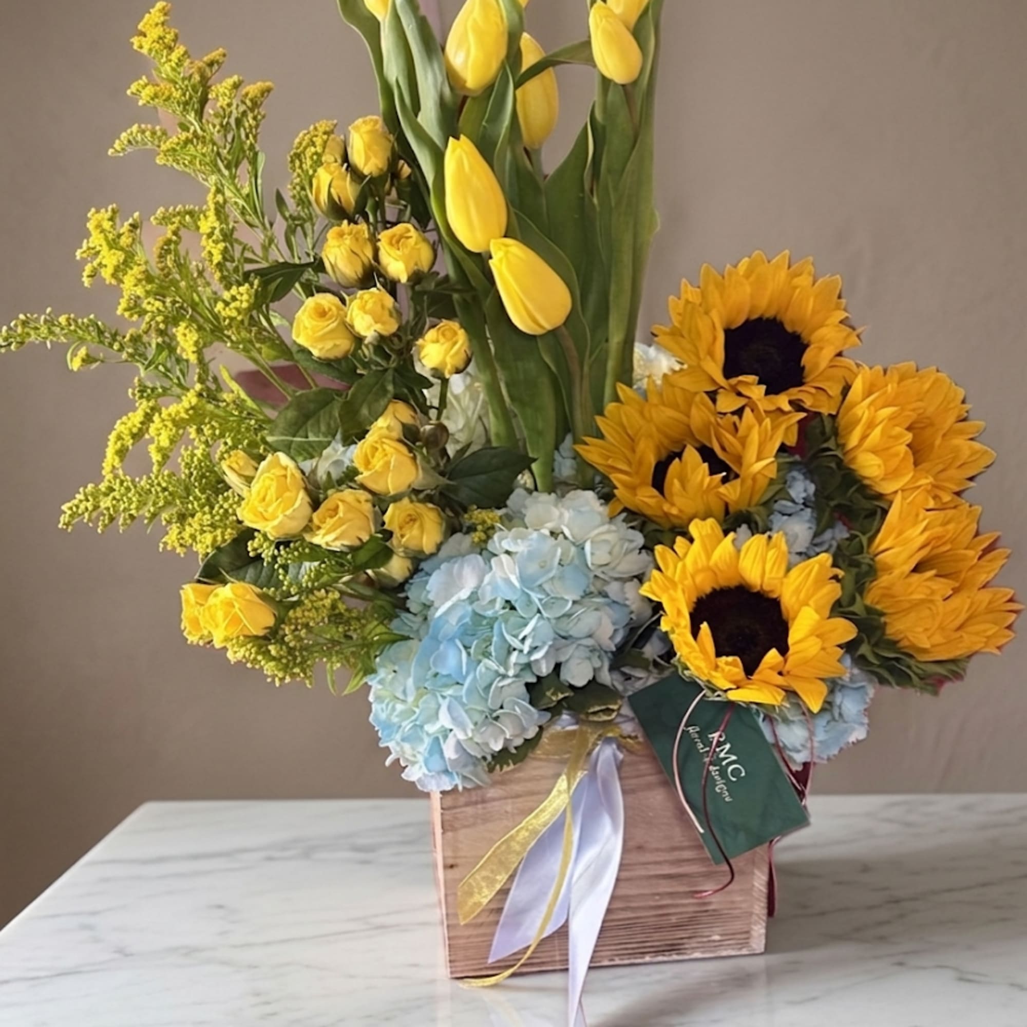 Yellow tulips, roses, sunflowers, and blue hydrangeas in a wooden box