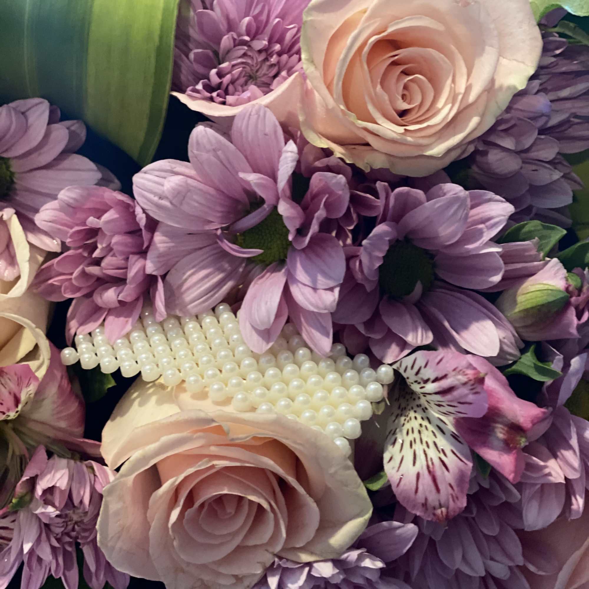 Pink roses and purple daisies with pearl accents in a bouquet