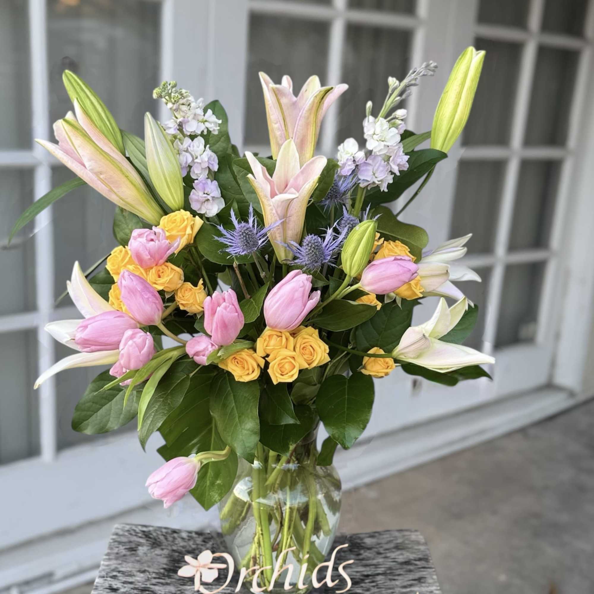 Bouquet of pink tulips, yellow roses, and lilies in a glass vase