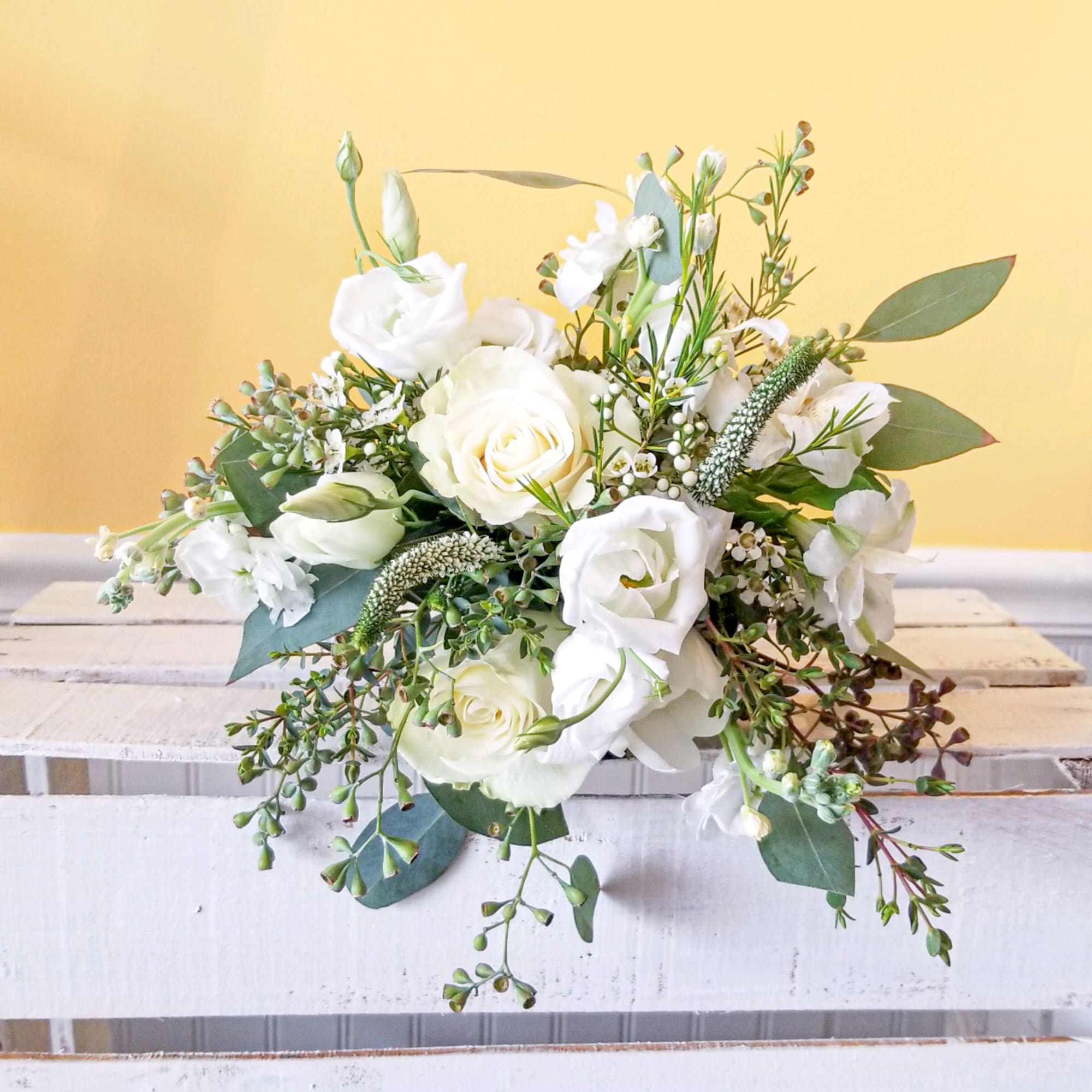 White roses and lisianthus arranged with greenery in a low bouquet.