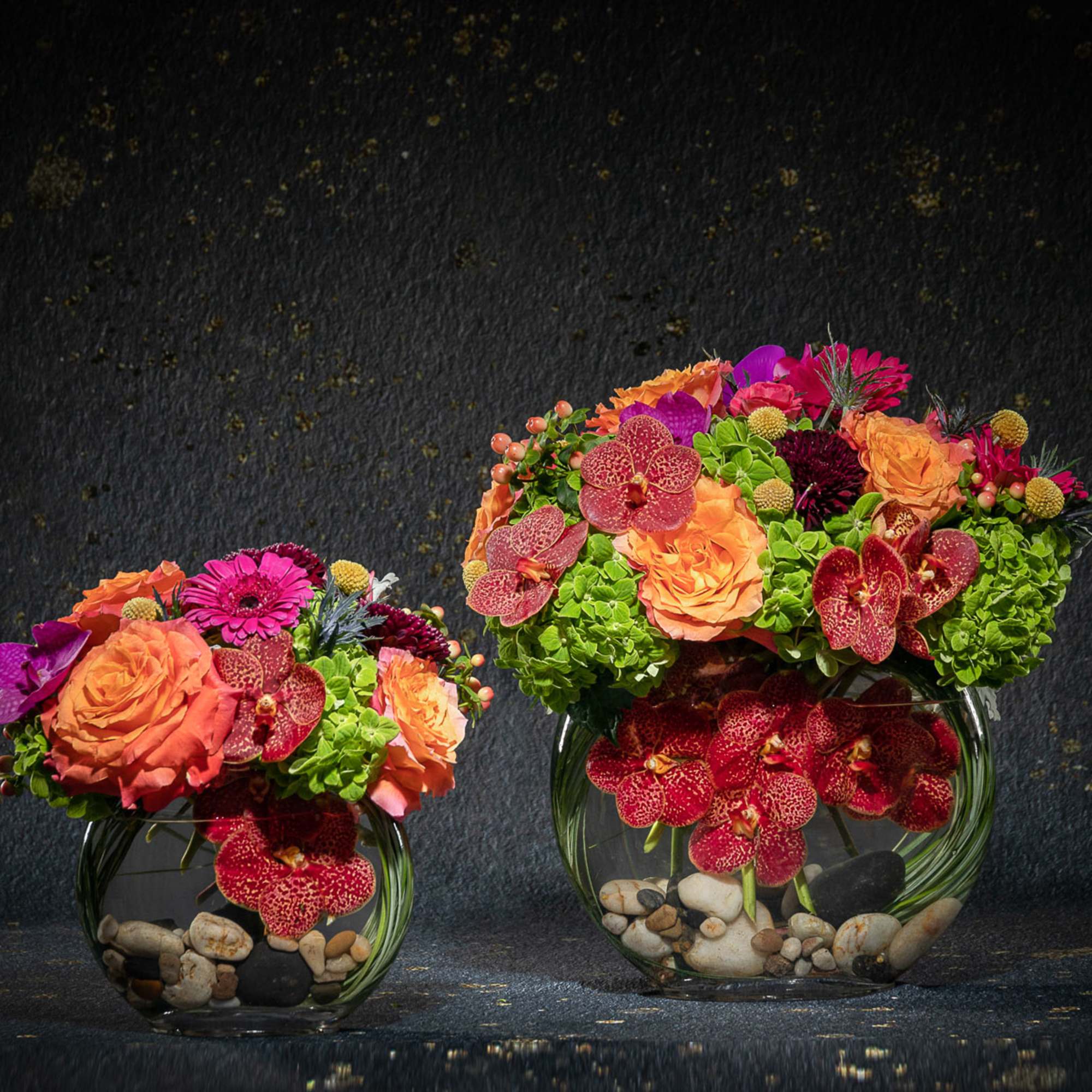 Two colorful floral arrangements in round glass vases with stones