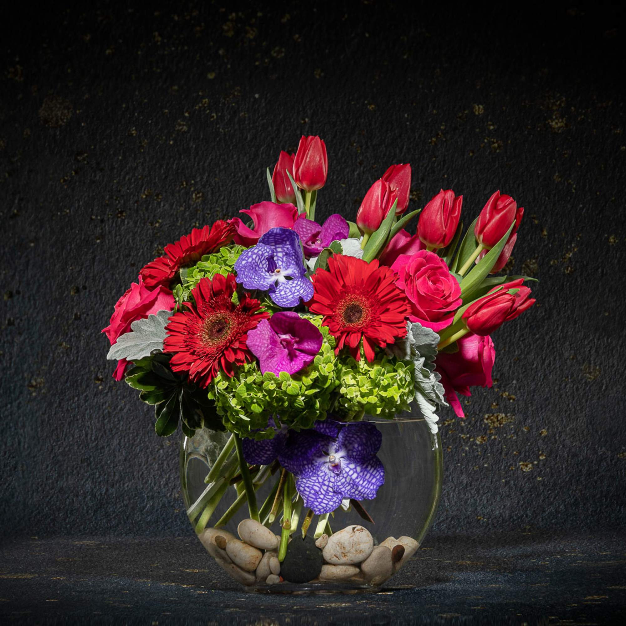 Bright mixed bouquet in a round glass vase with stones
