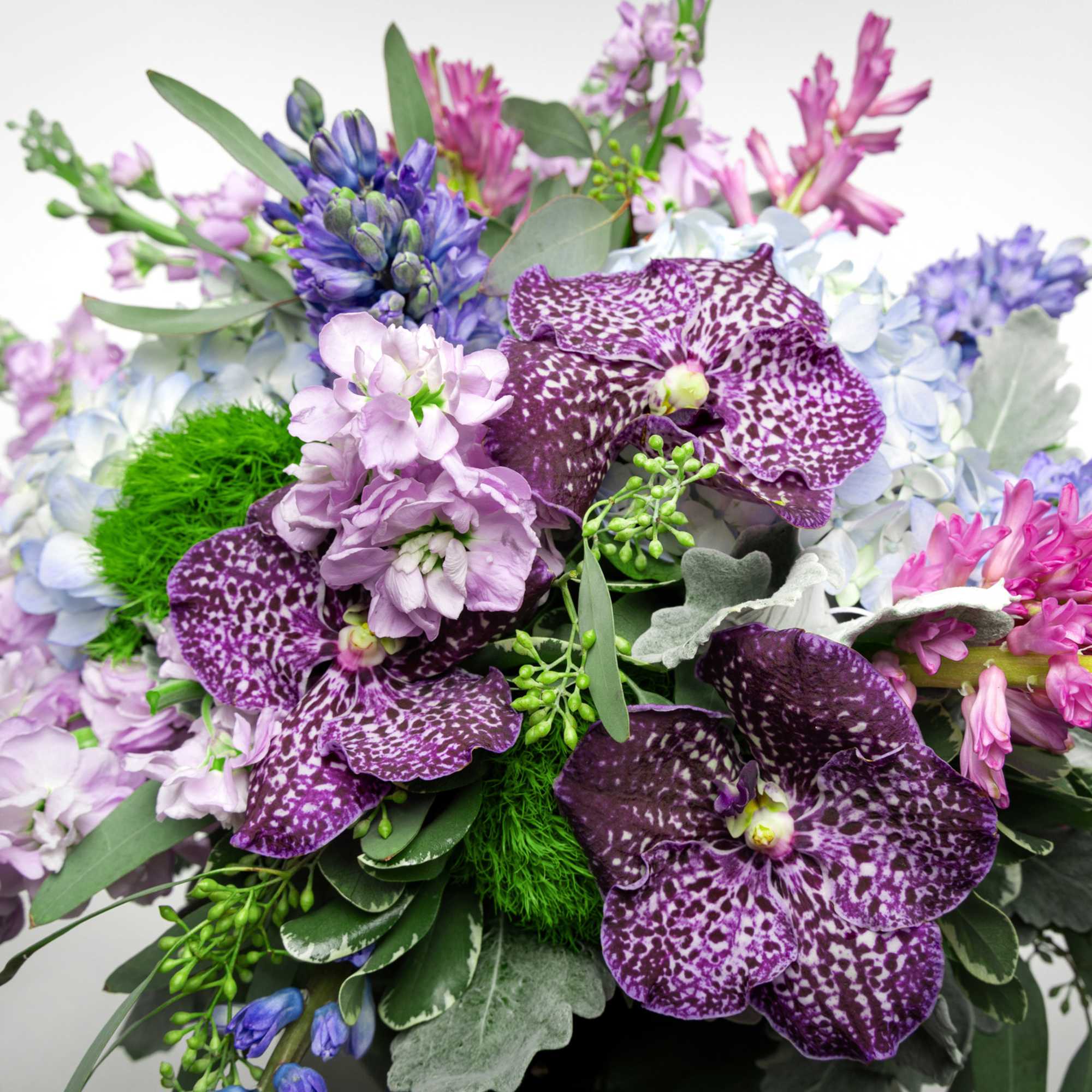 Purple and pink orchid bouquet with blue hydrangeas and greenery