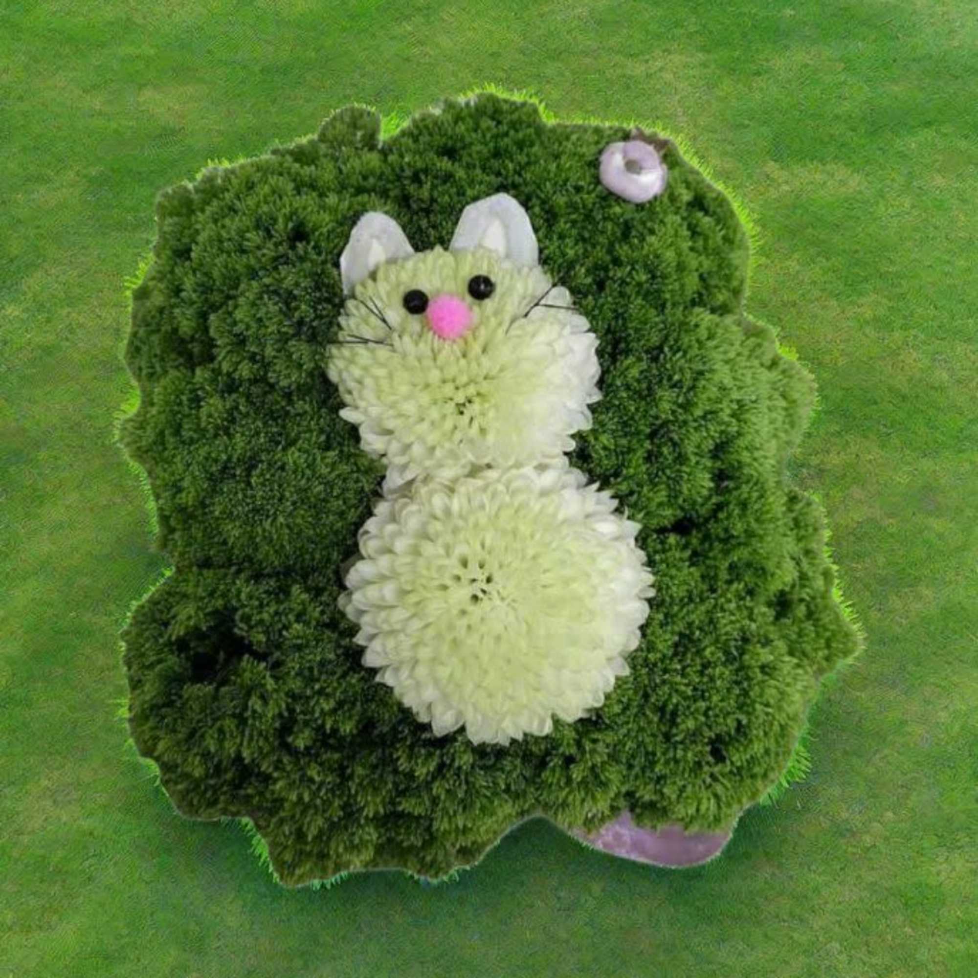 Novelty floral bunny made of white blooms resting on a square green moss cushion.