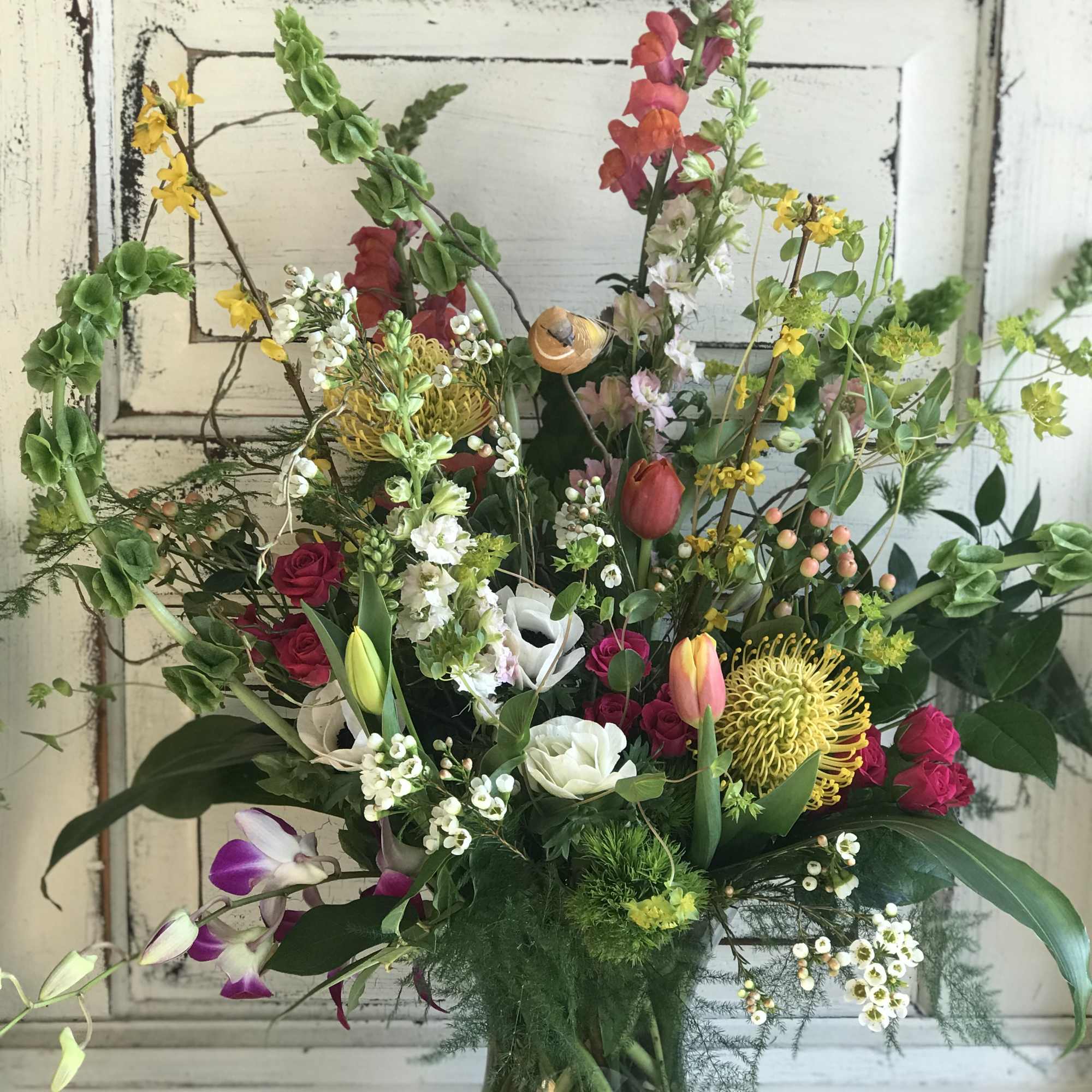 Mixed bouquet in a glass vase with roses, tulips, orchids, and yellow blooms
