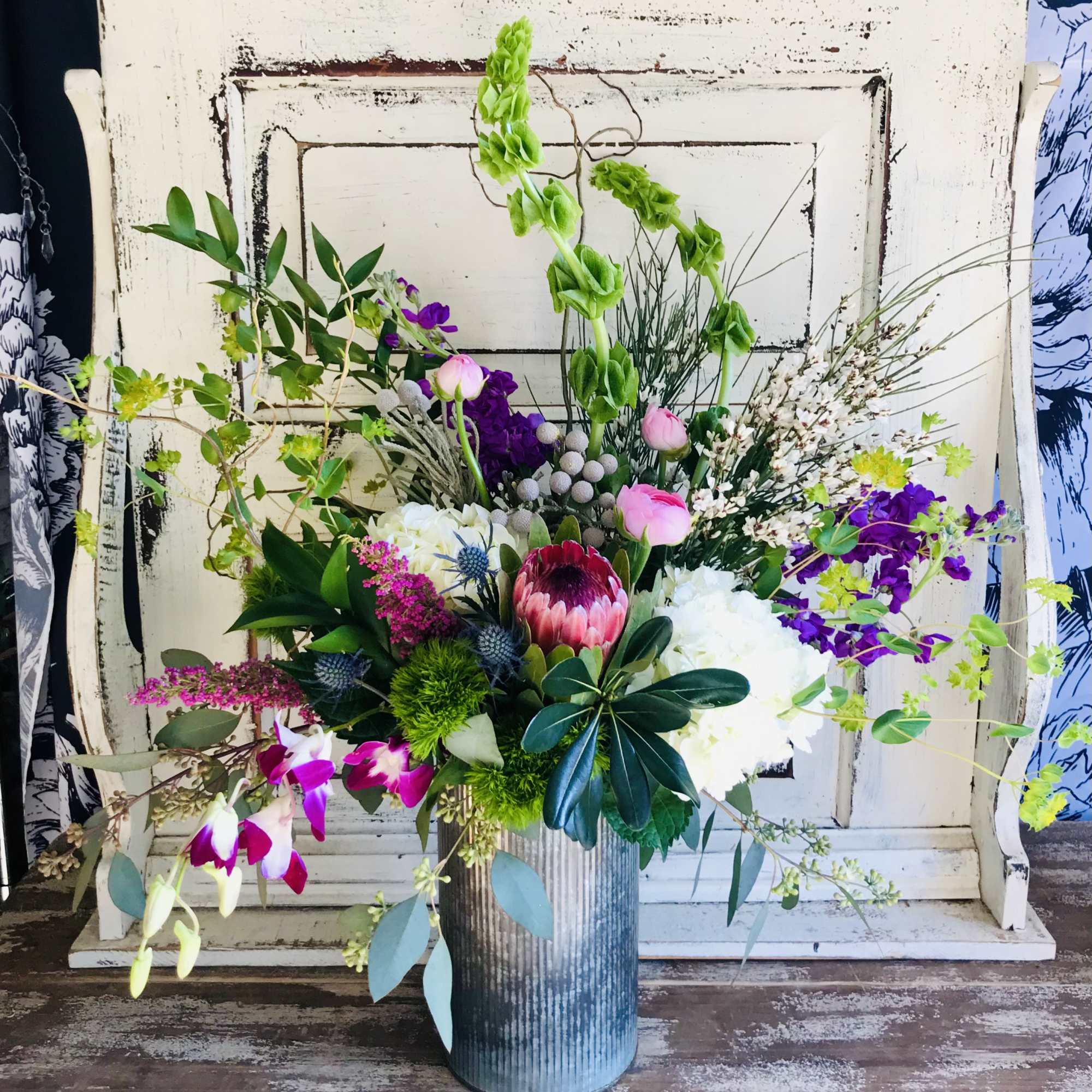 Tall mixed floral arrangement in a ribbed metal vase with pink, purple, white, and green blooms