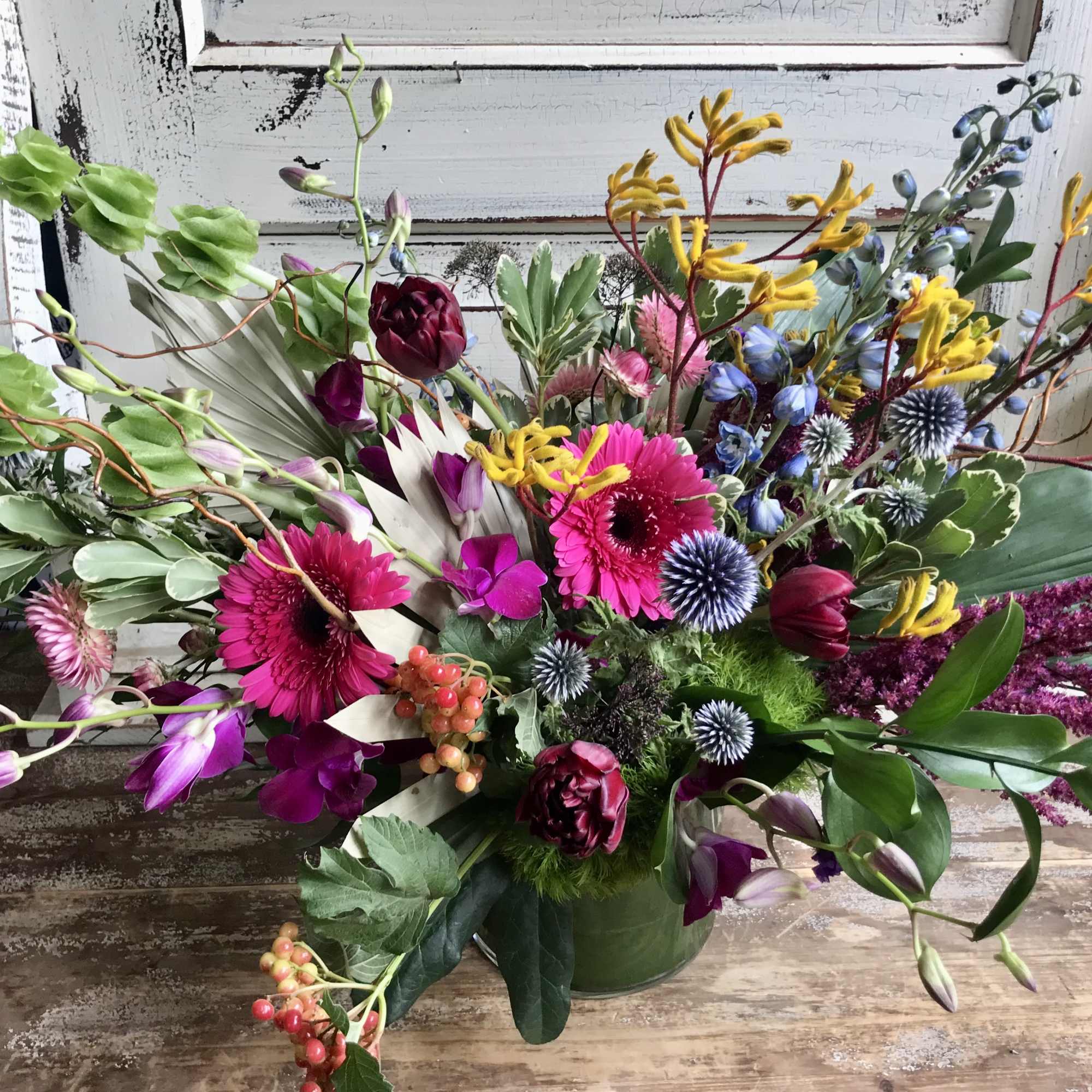 Colorful mixed floral arrangement in a green vase with pink, purple, yellow, and blue blooms