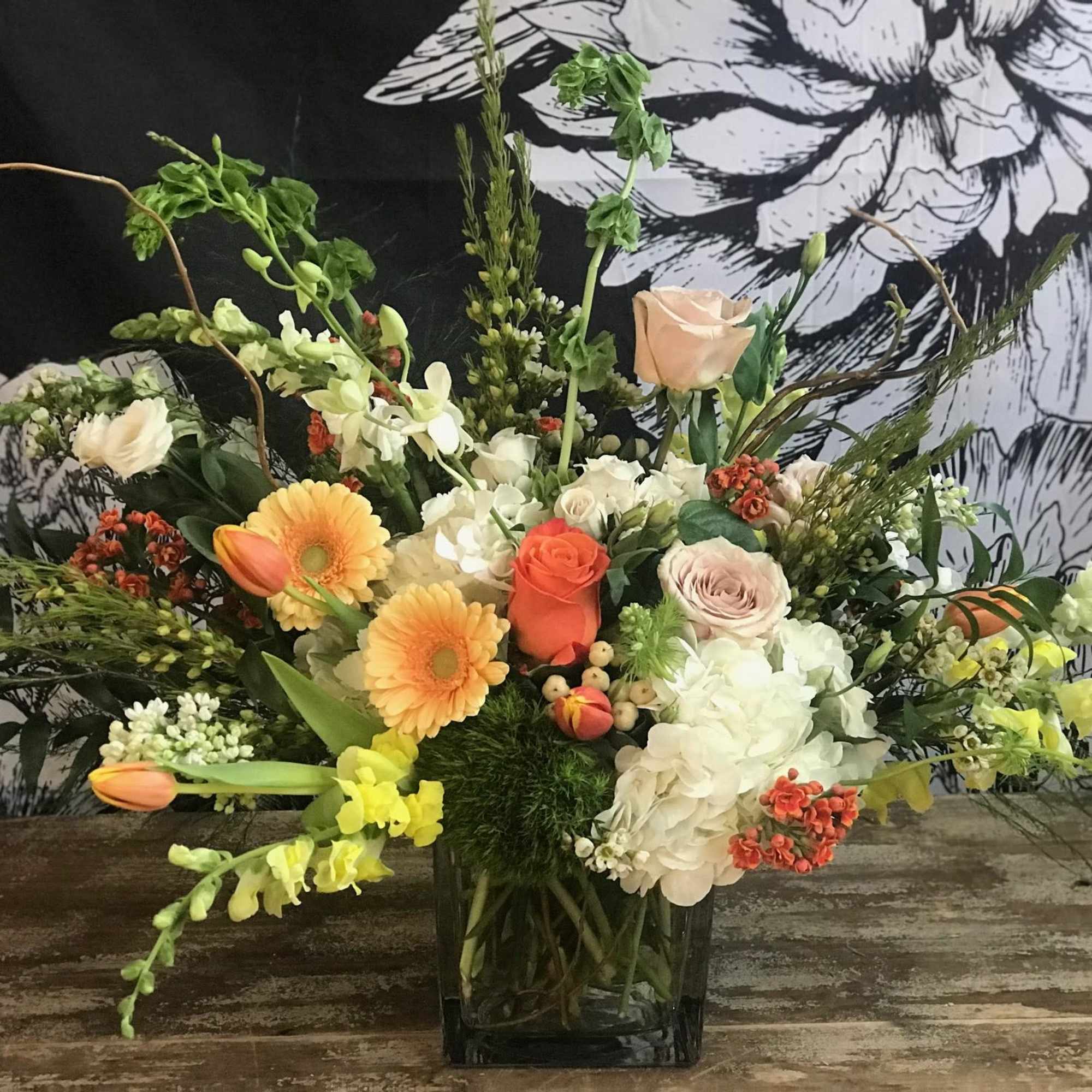 Mixed floral arrangement in a square glass vase with orange, white, and pale pink blooms