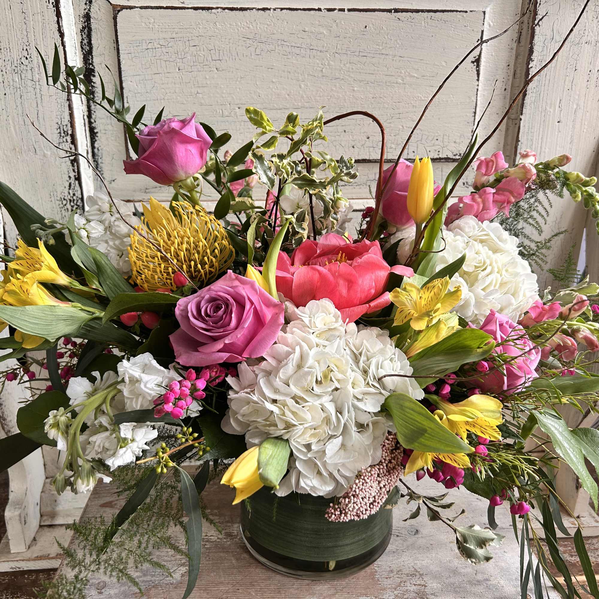 Mixed bouquet in a low green container with pink, white, and yellow flowers