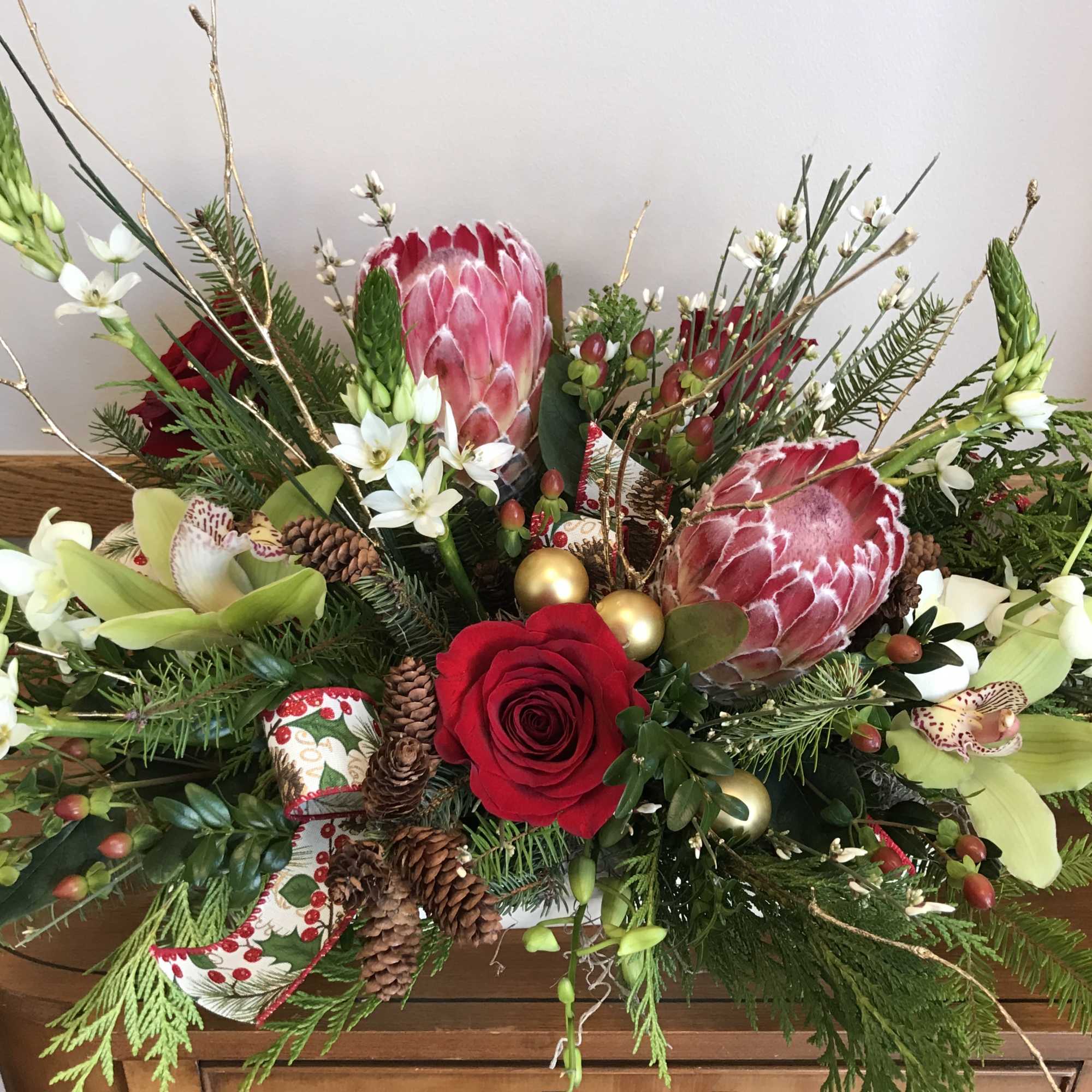 Holiday floral arrangement with red roses and protea in a low container