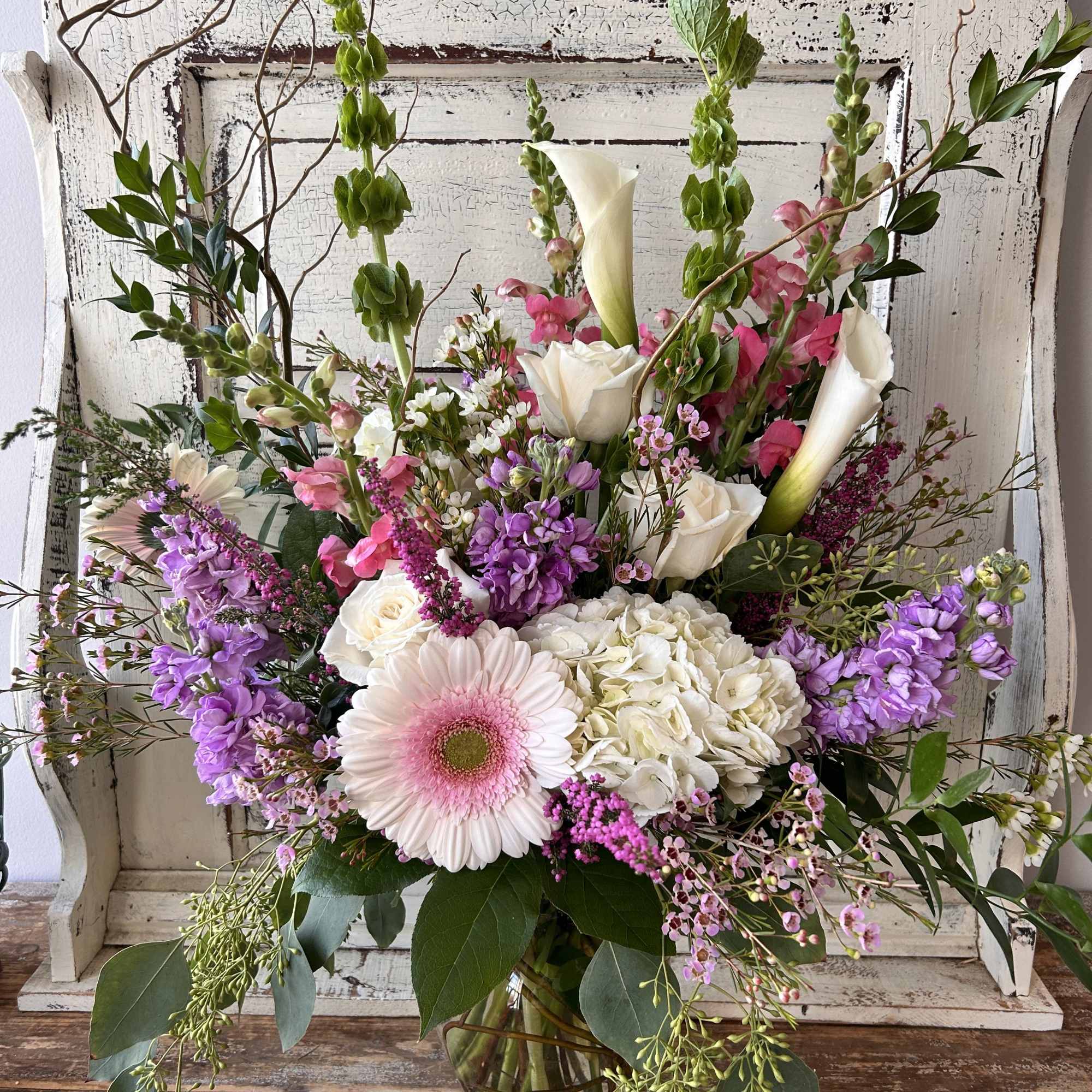 Mixed bouquet with pink gerbera, white calla lilies, and purple blooms in a glass vase
