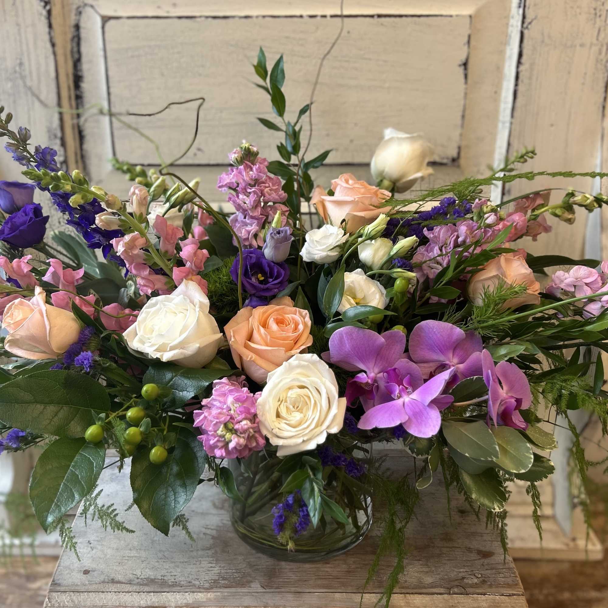 Mixed bouquet of roses, orchids, and pink blooms in a glass vase