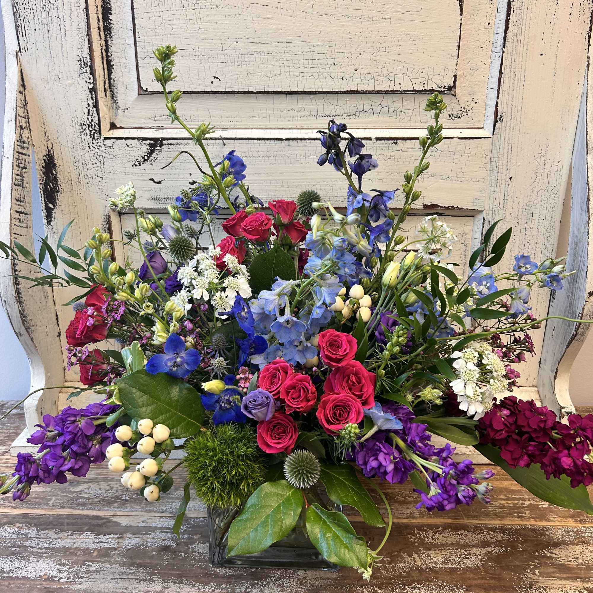 Mixed bouquet of pink roses, blue delphinium, and purple flowers in a glass vase