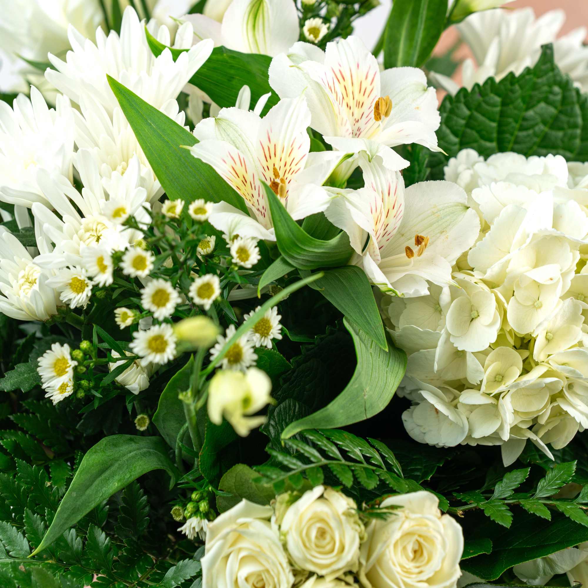 White flowers including lilies, roses, and hydrangeas in a green bouquet