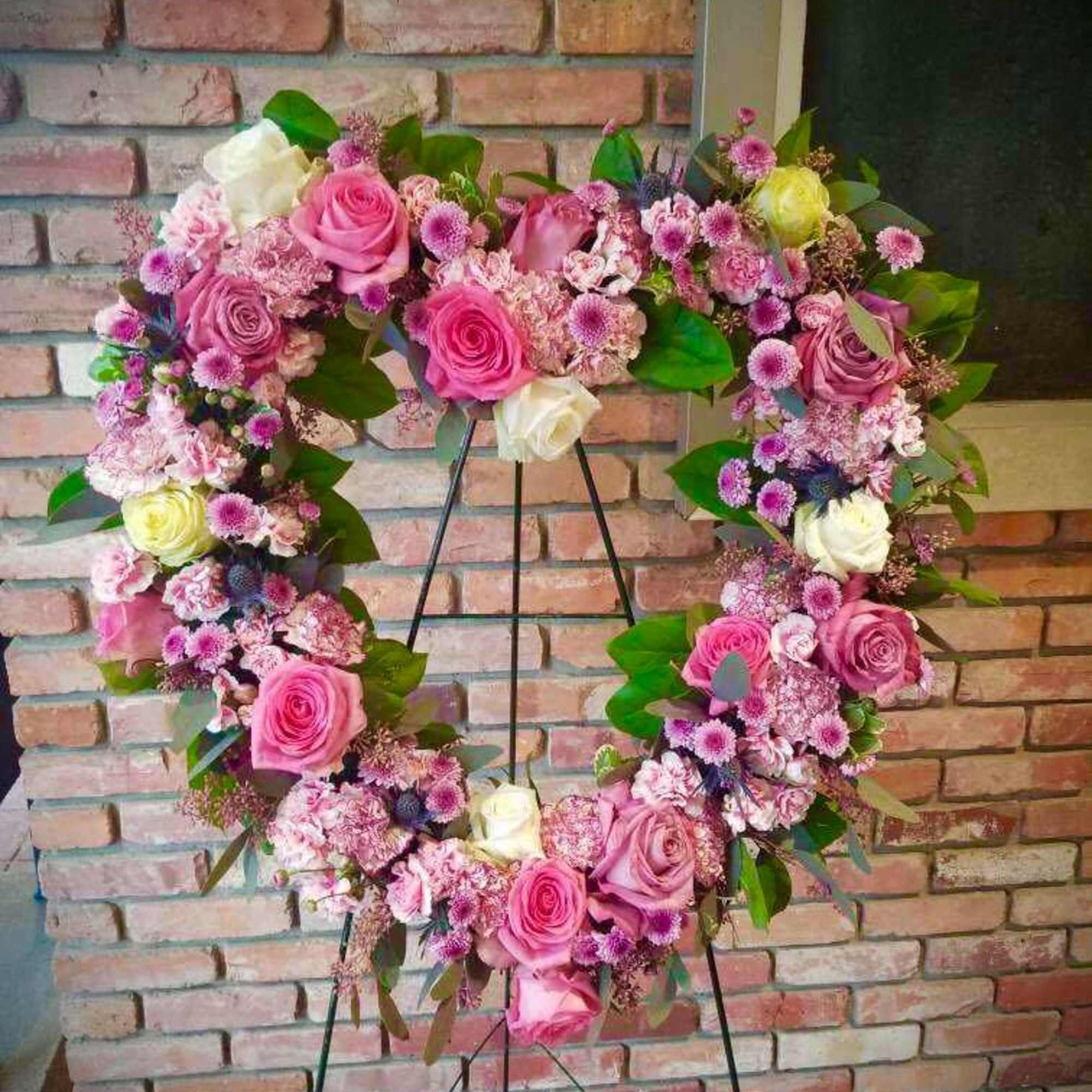 Heart-shaped floral wreath with pink and white roses on a stand