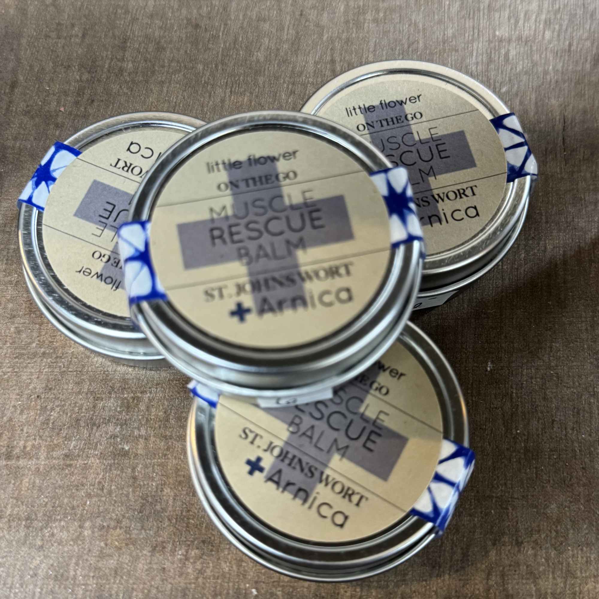 Four small tins of muscle rescue balm on a wooden surface