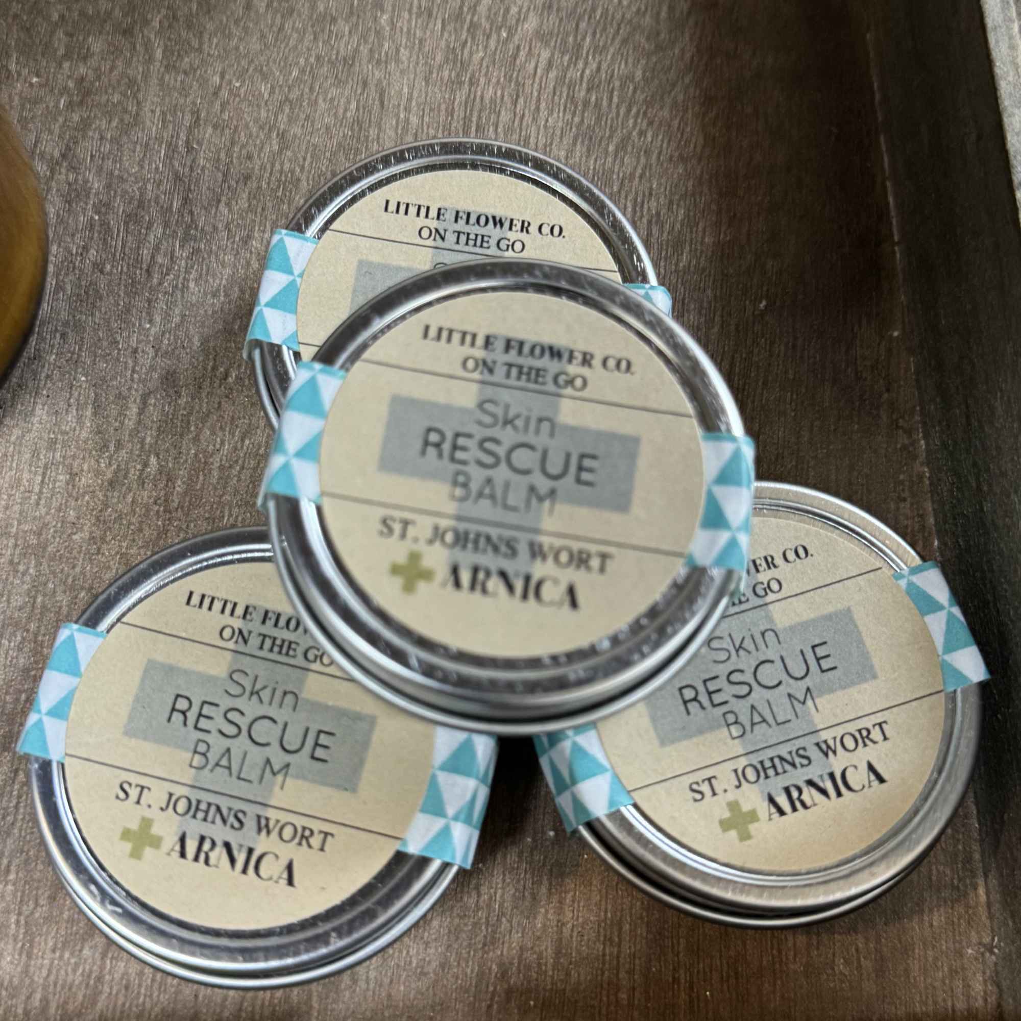 Three tins of skin rescue balm stacked in a wooden tray