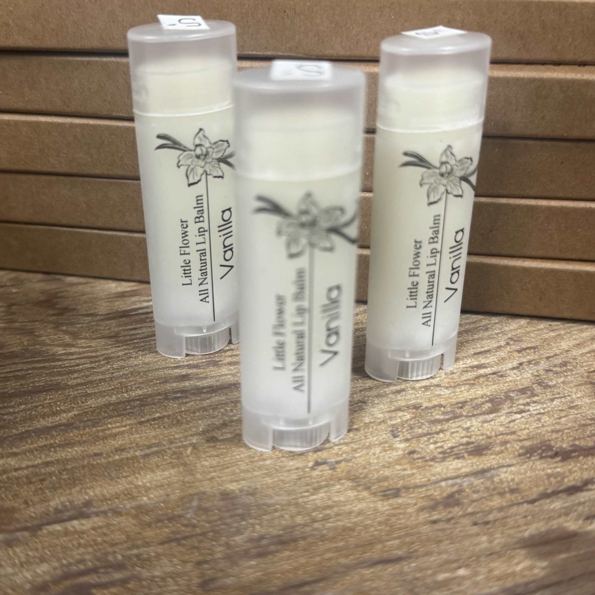 Three vanilla lip balm tubes on a wooden surface