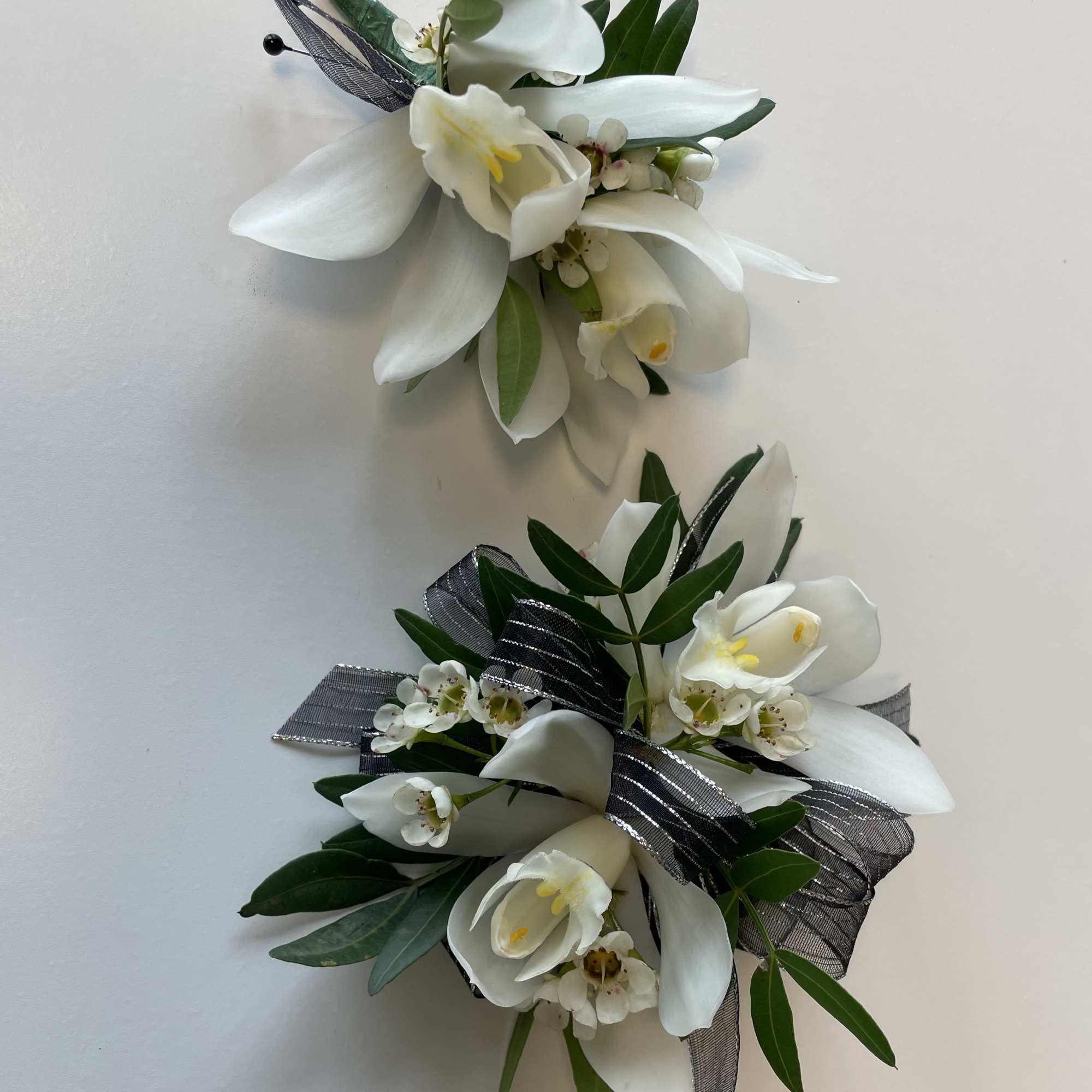 White floral corsages with ribbon and greenery