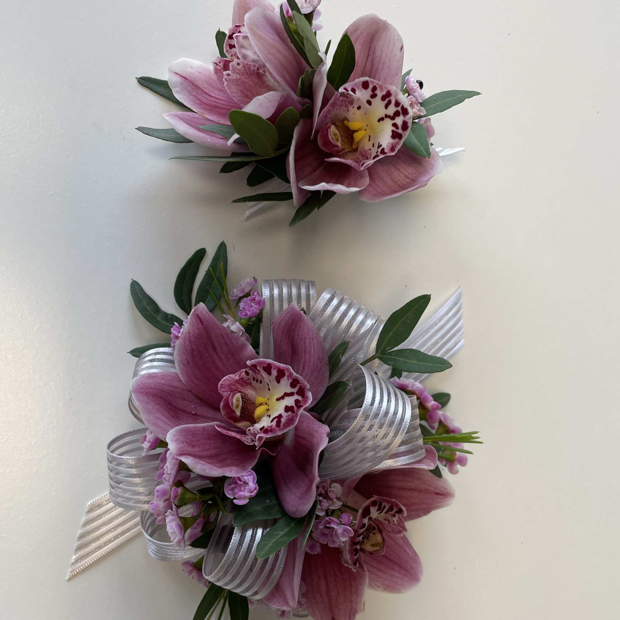 Two pink orchid corsages with silver ribbon and greenery