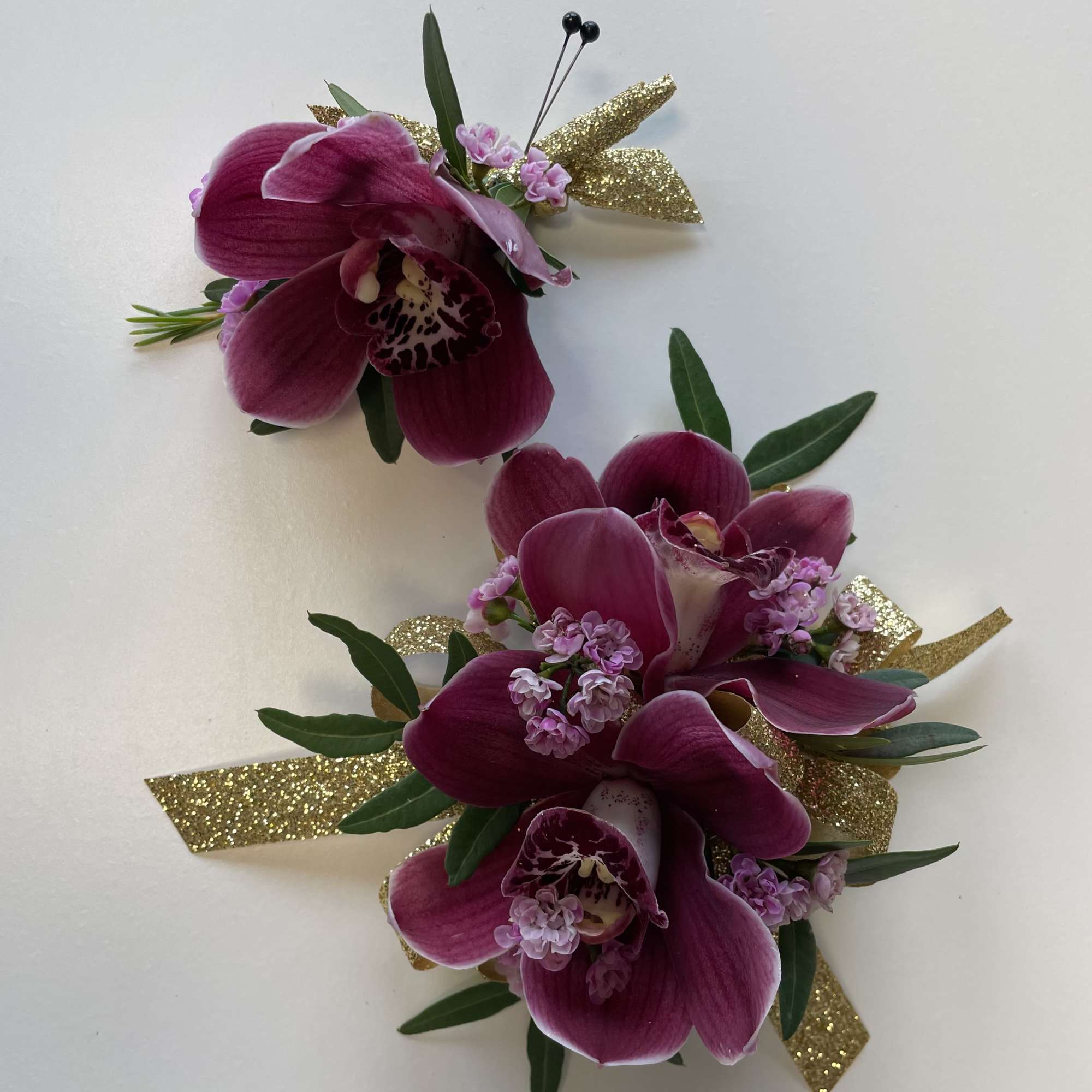 Two magenta orchid corsages with gold glitter ribbon accents