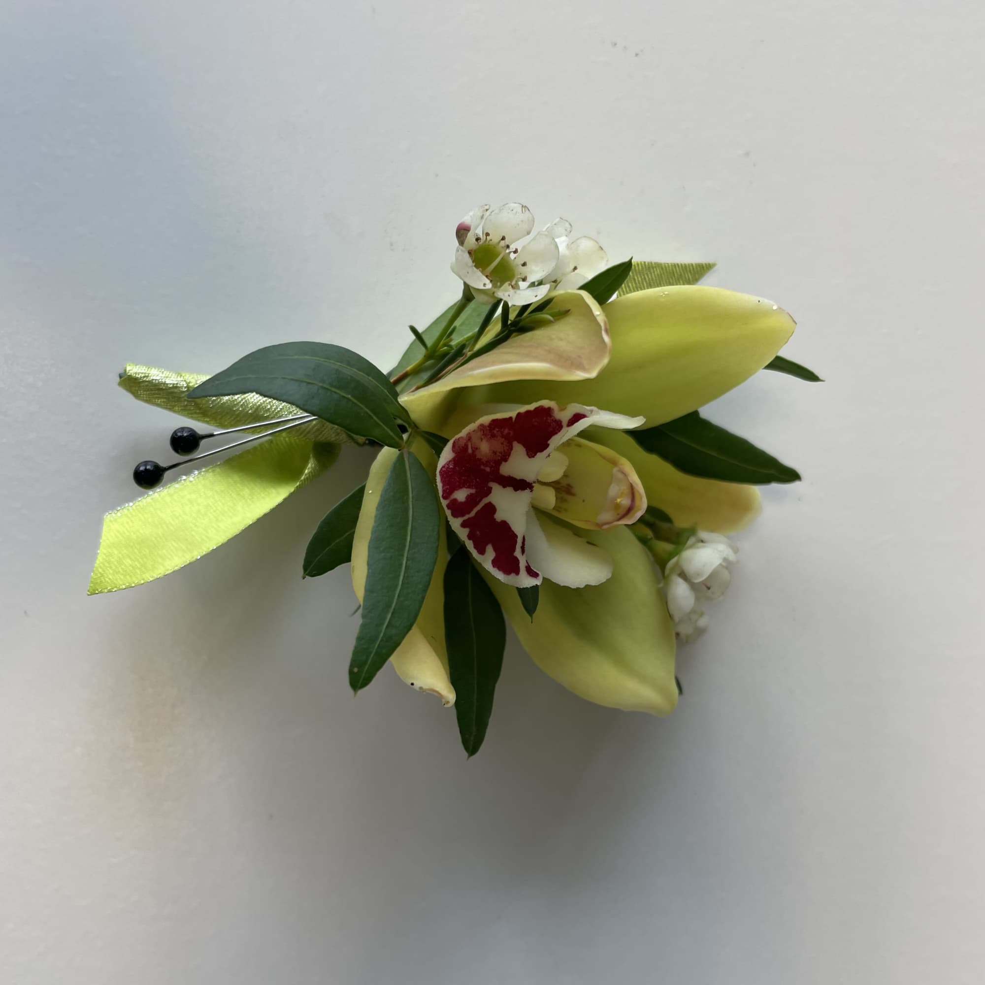 Small floral corsage with pale yellow blooms and green ribbon