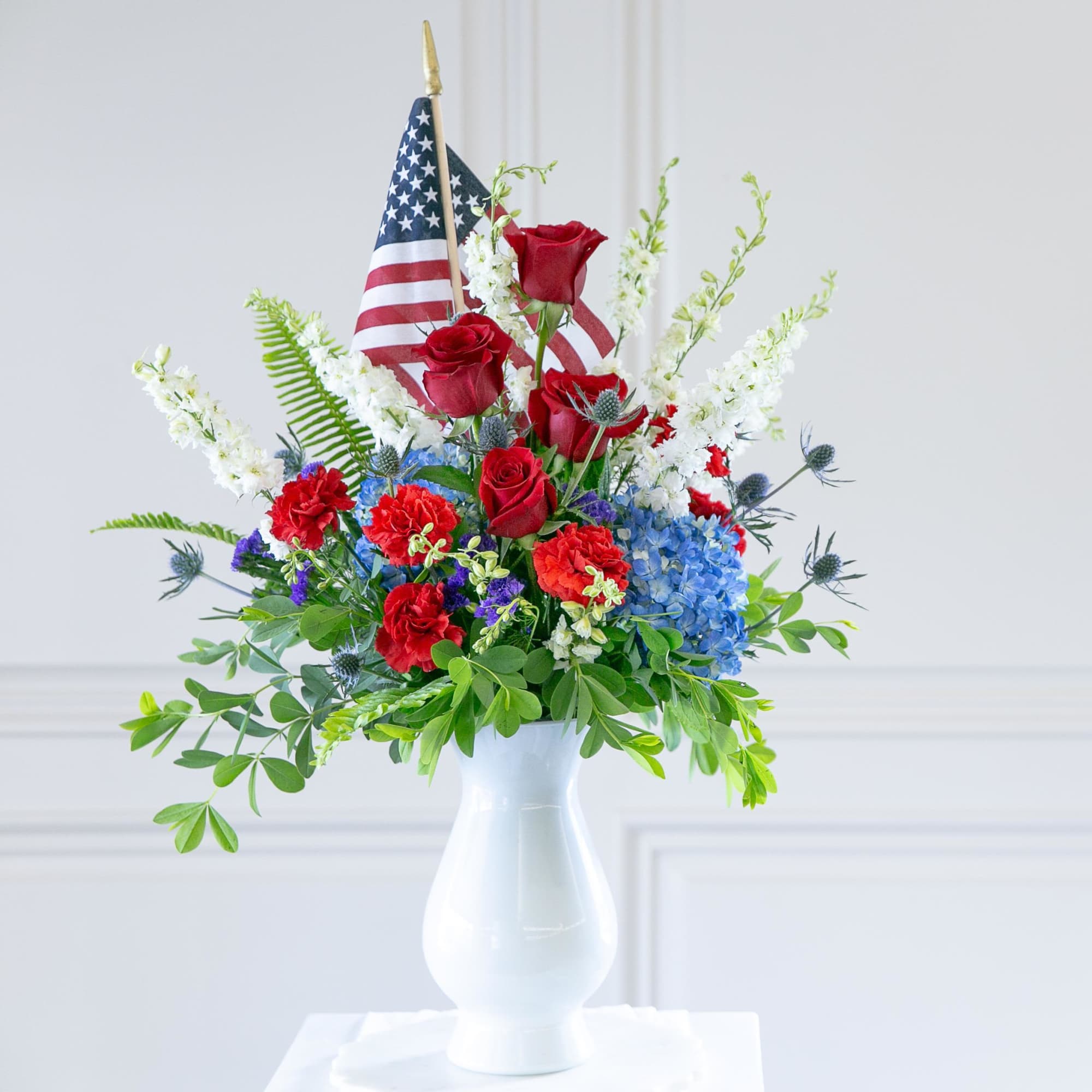 Red roses and blue hydrangeas in a white vase with an American flag