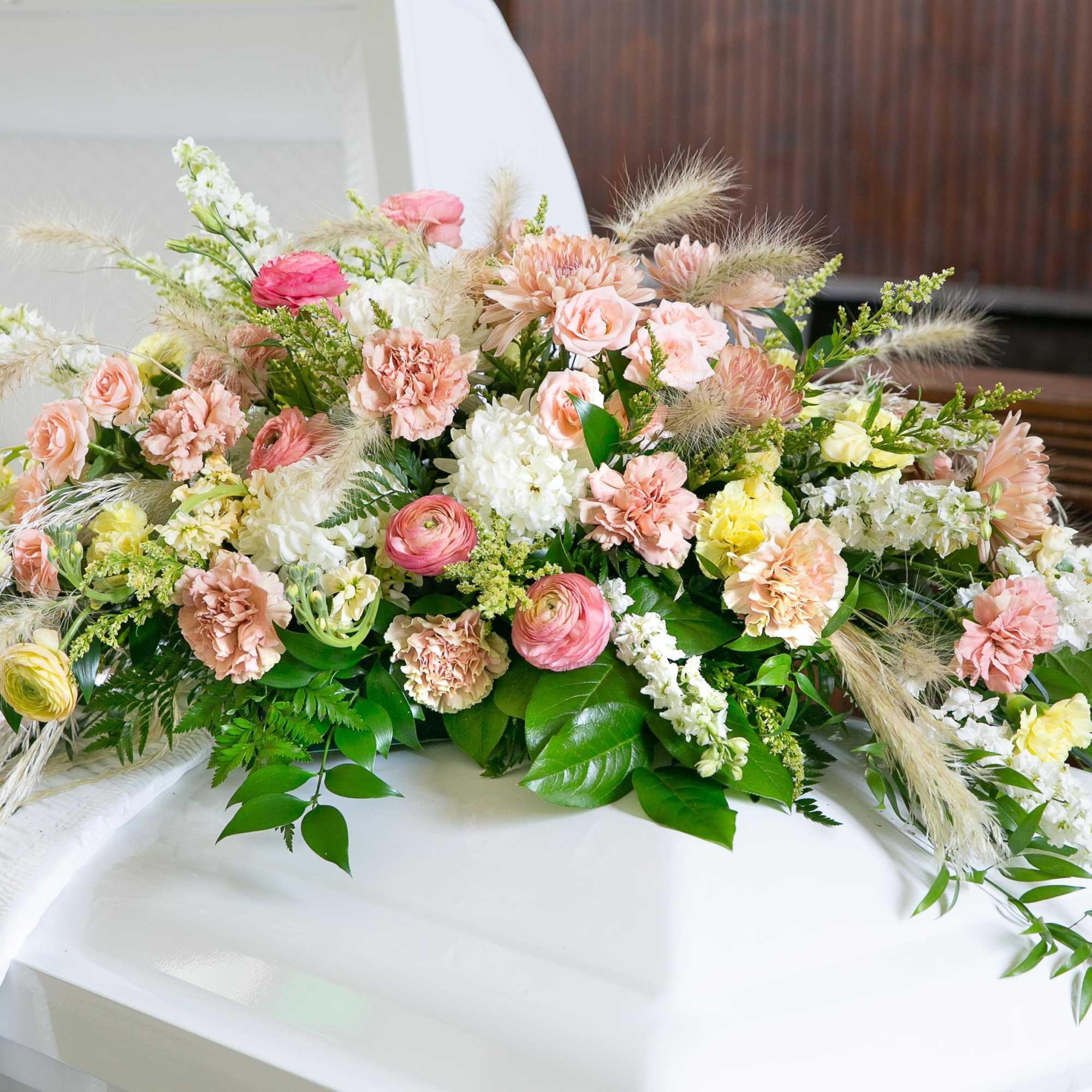 Pastel floral casket spray with pink, peach, and white blooms
