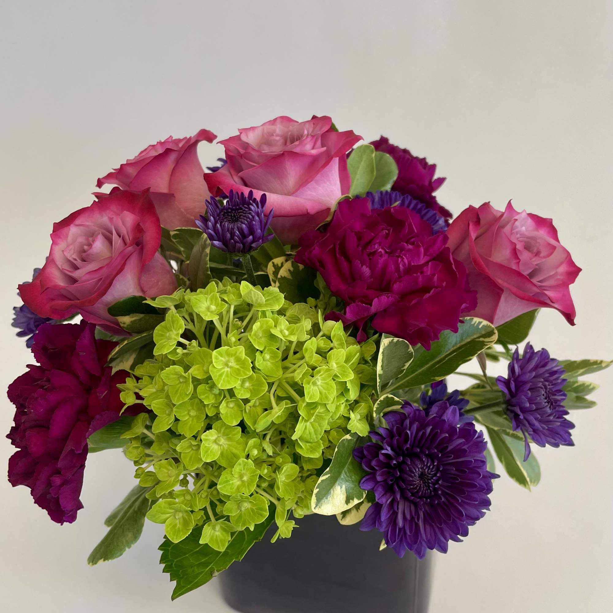 Pink roses and purple flowers in a black square vase