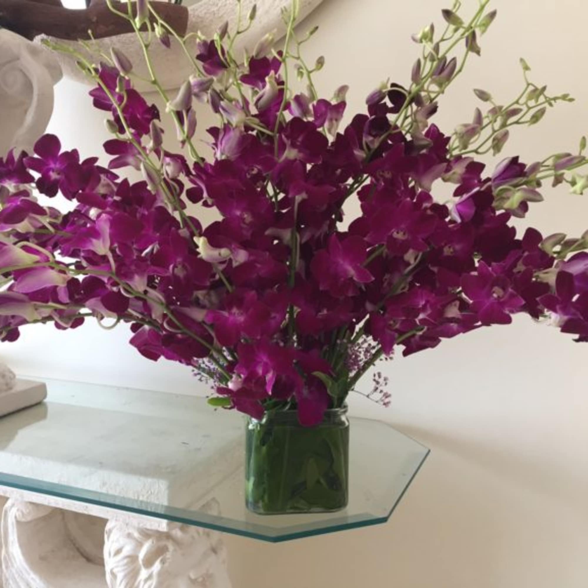 Spray of bright purple dendrobium orchids arranged in a low square glass vase.