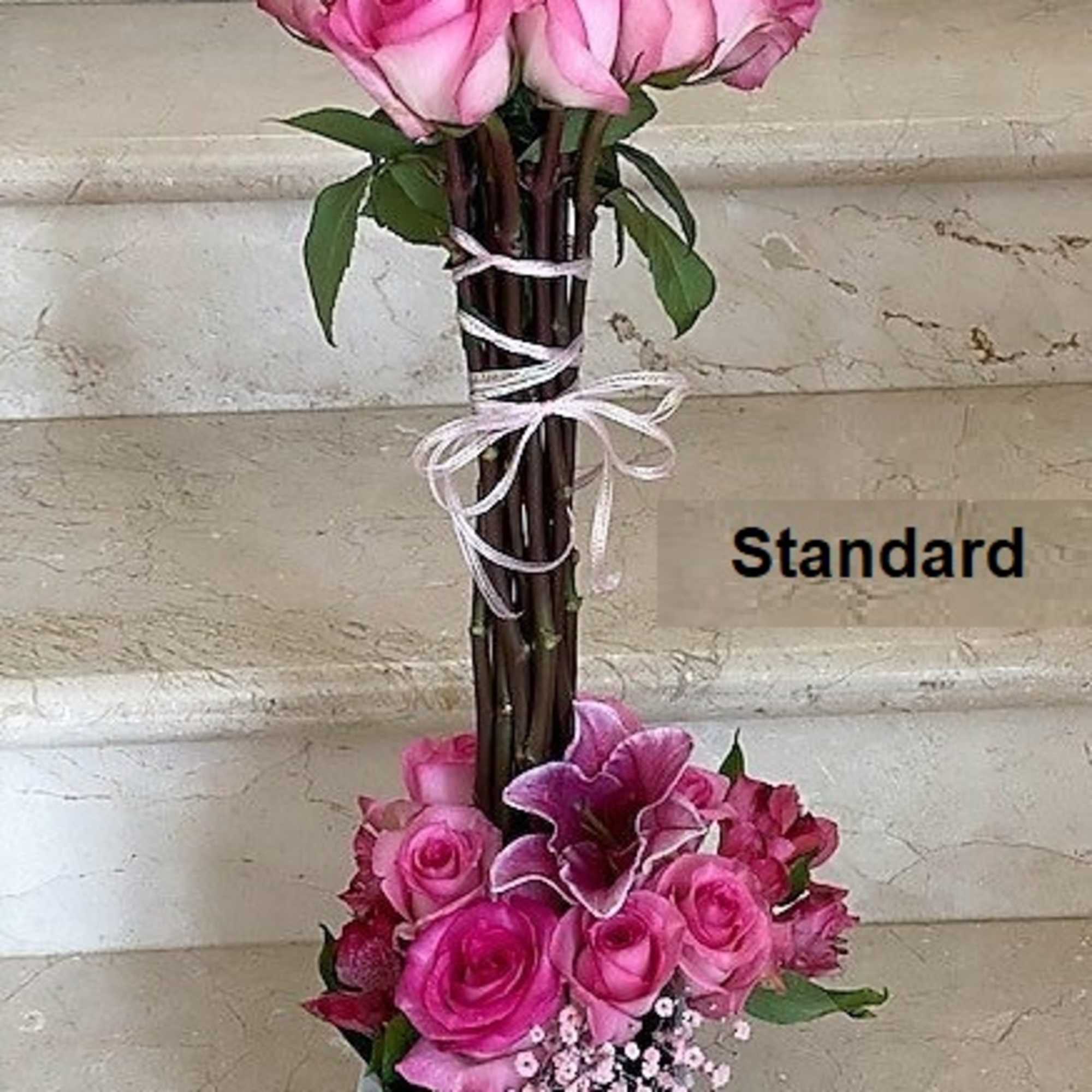 Tall arrangement of pink roses and lilies in a white square vase with bundled stems tied with ribbon