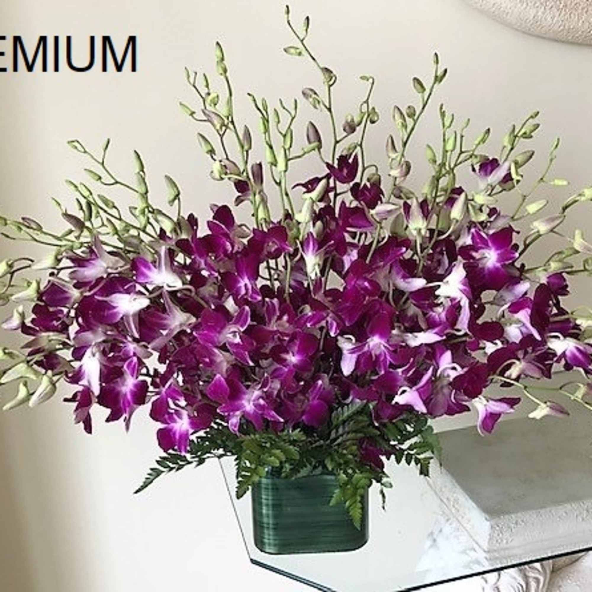 Large arrangement of purple and white orchids in a low green glass vase