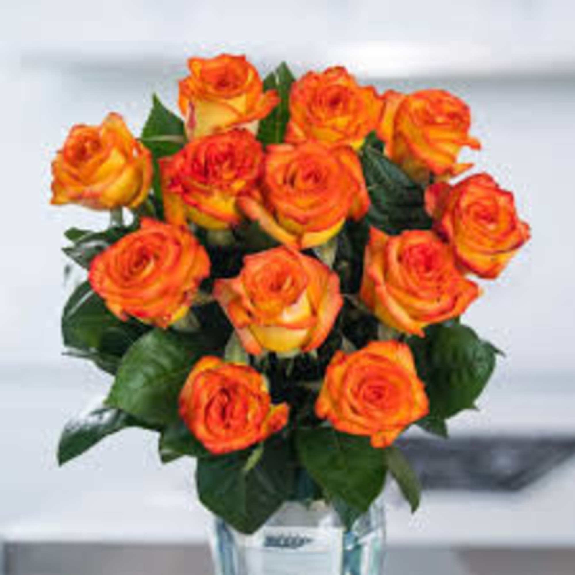 Vase of orange and yellow roses arranged in a rounded bouquet