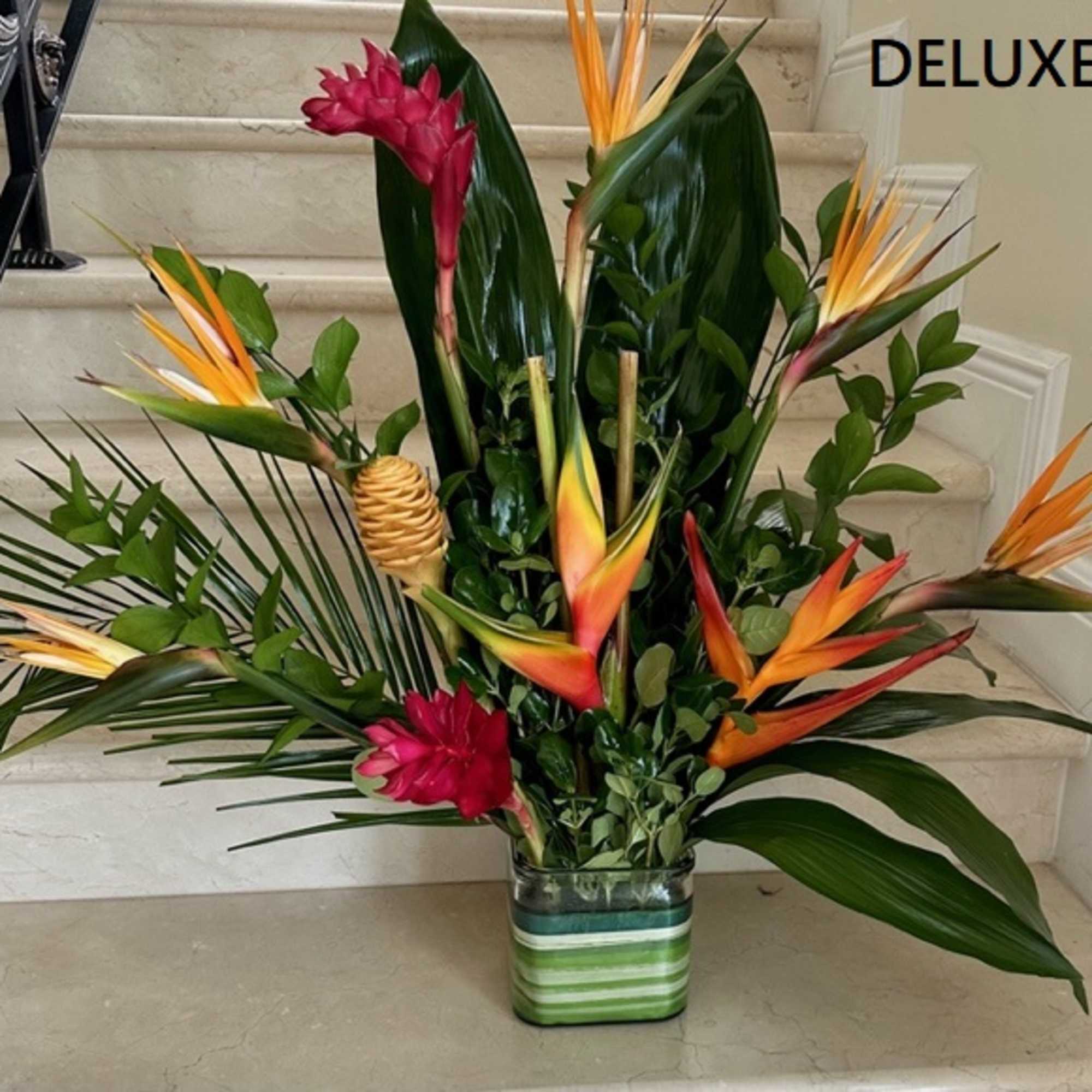 Tall tropical arrangement with orange and red blooms in a striped green glass vase
