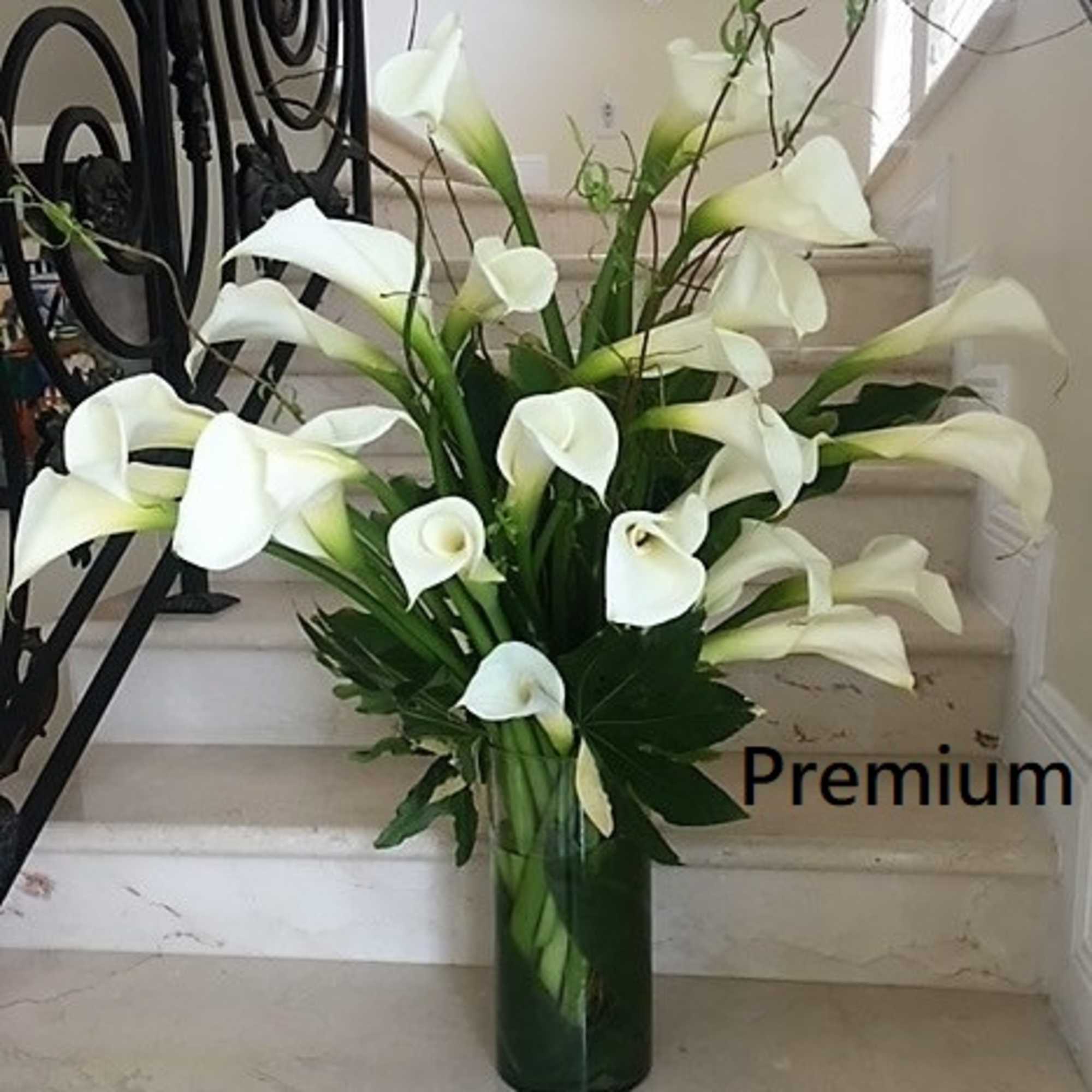 Tall arrangement of white calla lilies in a clear cylinder vase on a staircase