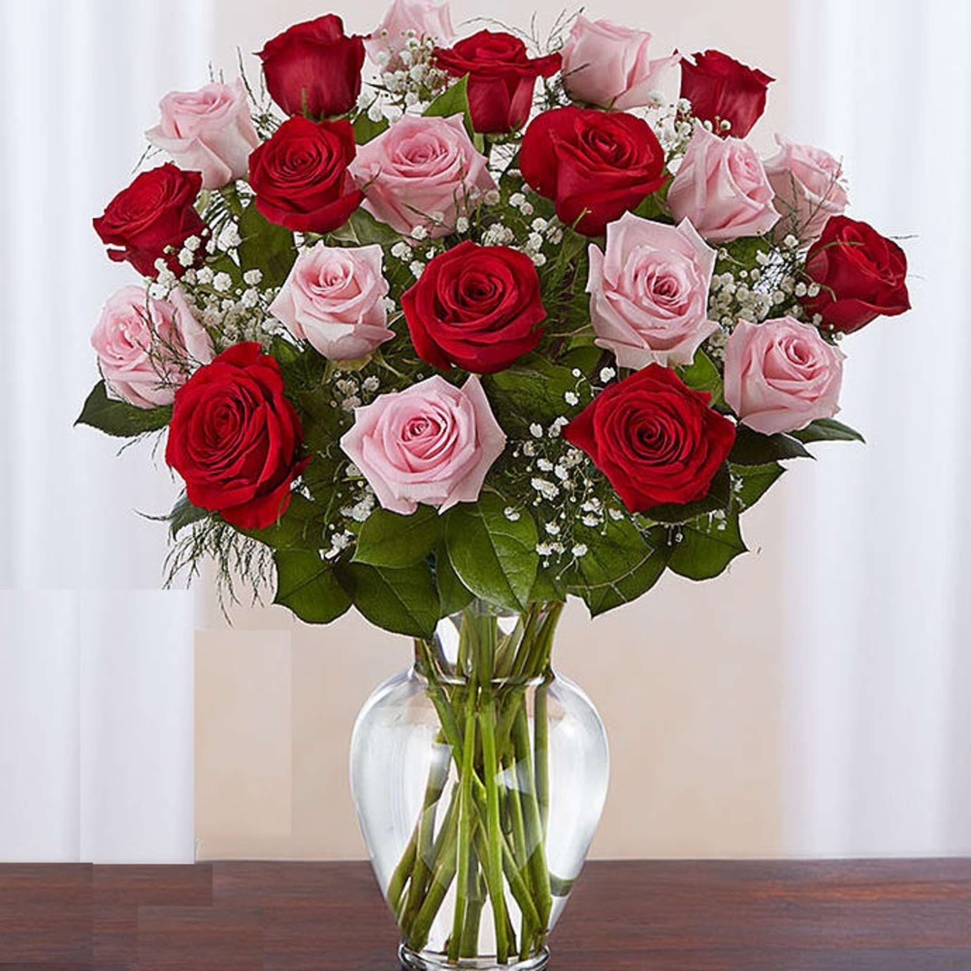 Arrangement of red and pink roses with white filler flowers in a clear glass vase