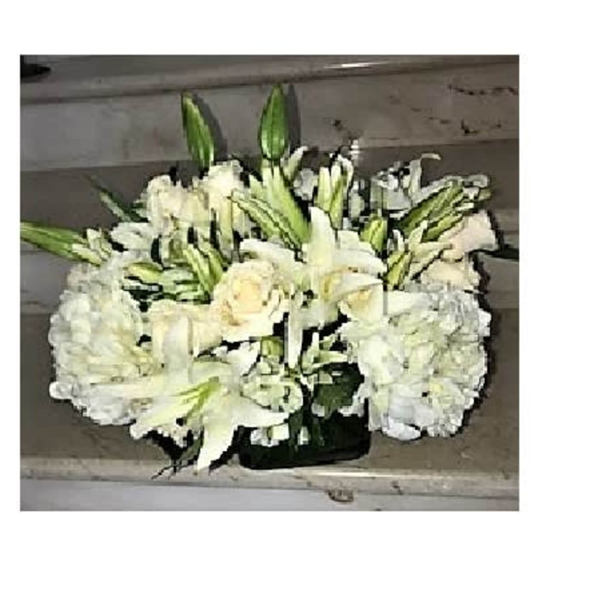 Low white arrangement of lilies, roses, and hydrangeas in a clear glass vase